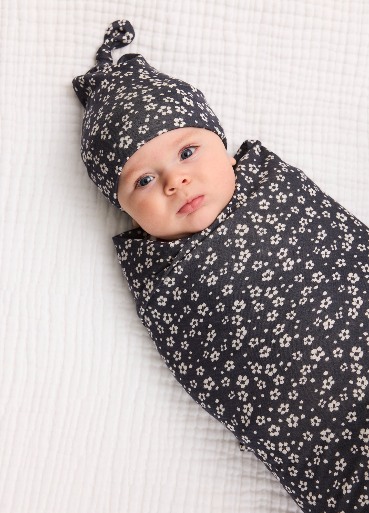 Black baby swaddle and knotted hat set with small white floral print on soft fabric.