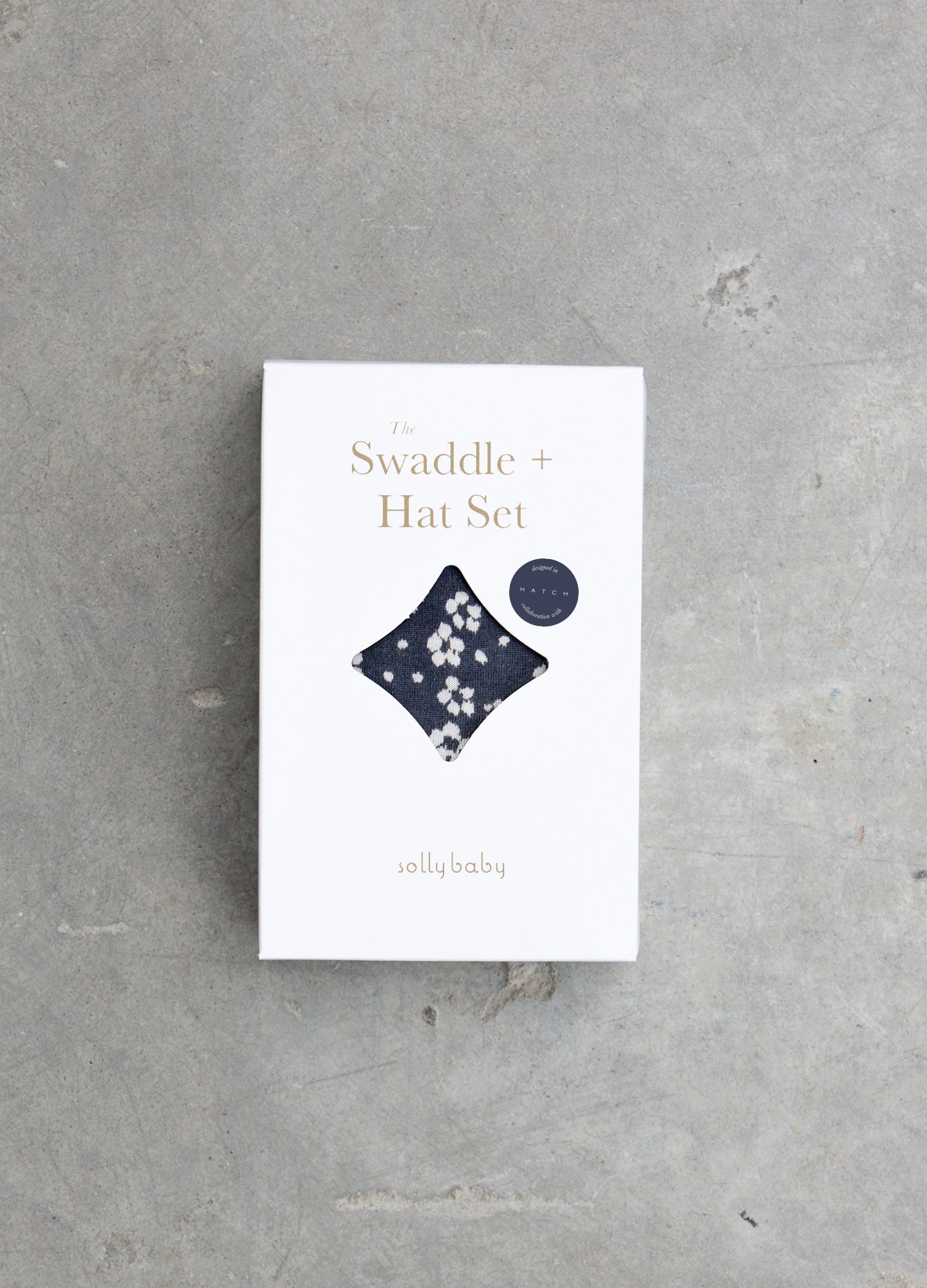 White packaging box featuring a navy blue floral baby swaddle and matching hat set illustration.