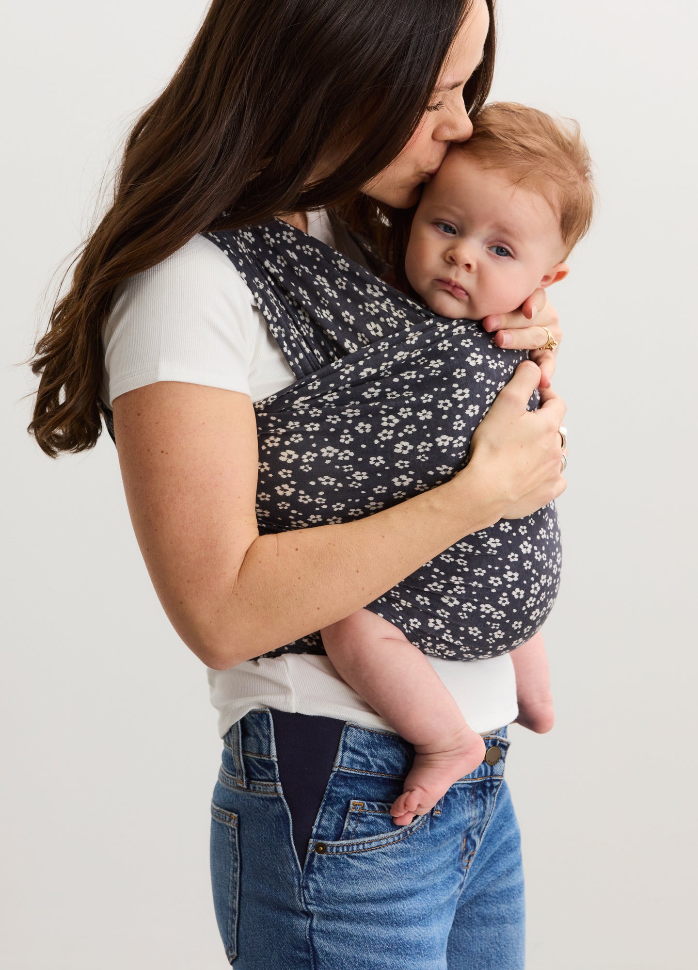 Navy blue baby wrap with white ikat bloom patterns worn by woman holding infant close.