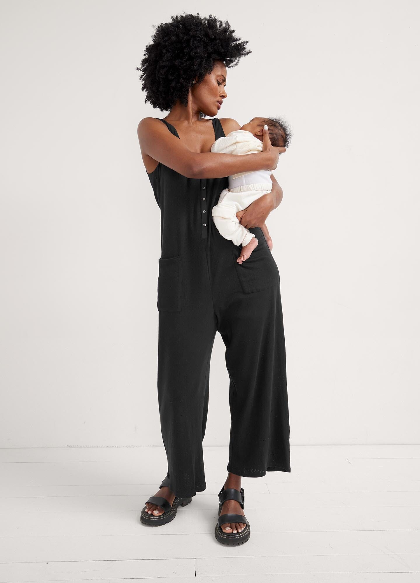 The 24/7 Feeding Jumpsuit - Black sleeveless maternity jumpsuit with button-front nursing access and relaxed fit for pregnancy and postpartum comfort.