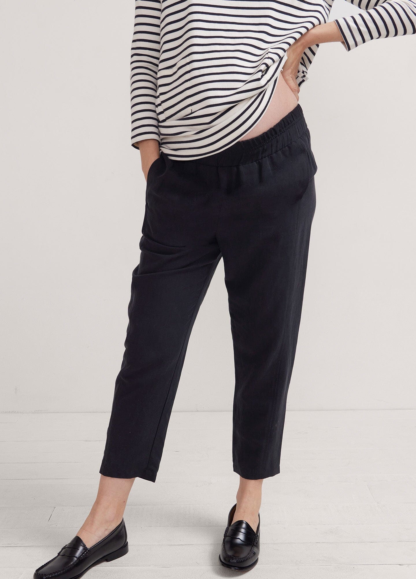 The Asher Pant - Black maternity pants with tapered legs, worn with a striped long-sleeve top, designed for pregnancy, nursing, and.