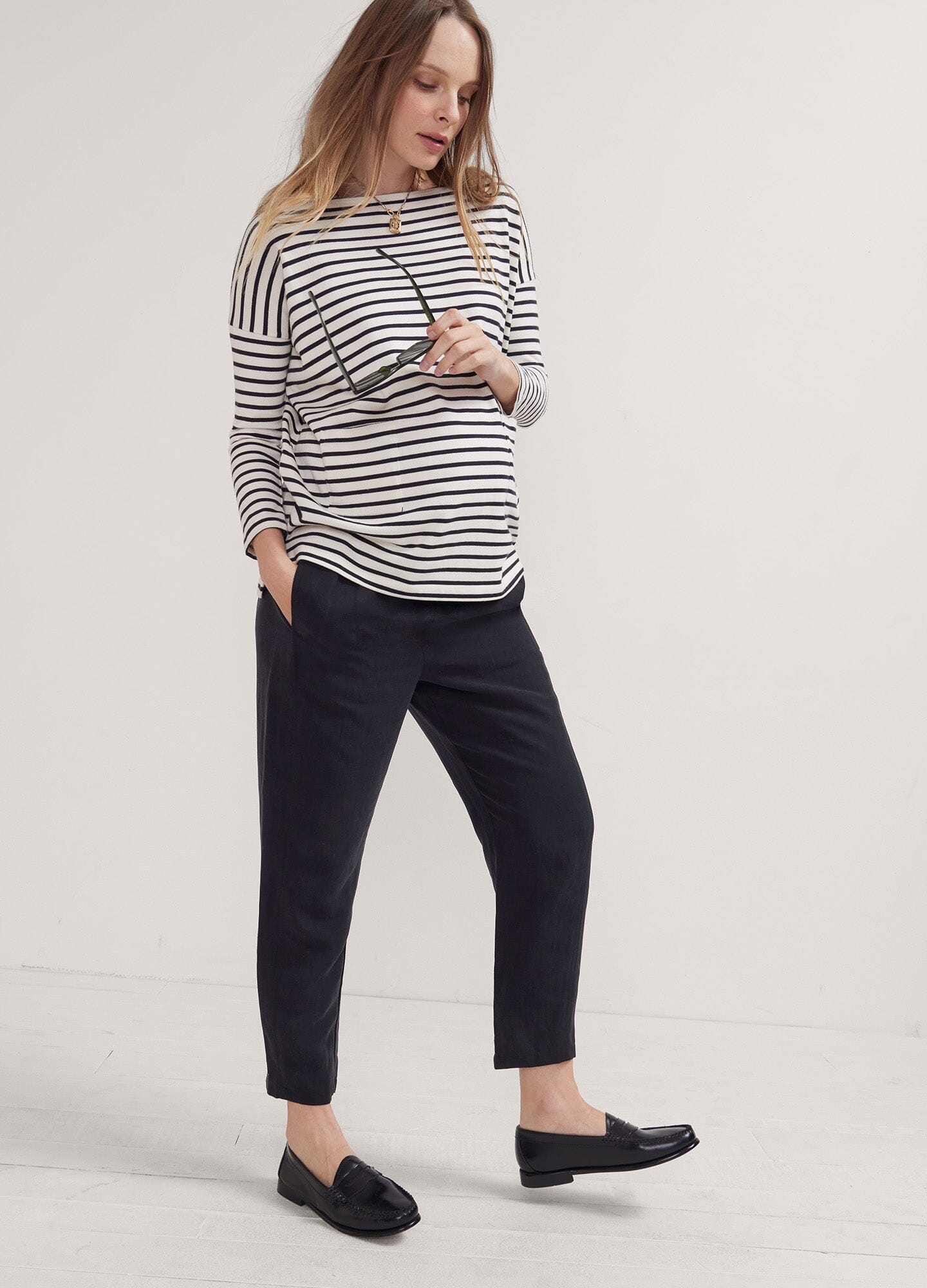 The Asher Pant - Black maternity pants with tapered legs, worn with a striped long-sleeve top, designed for pregnancy, nursing, and.