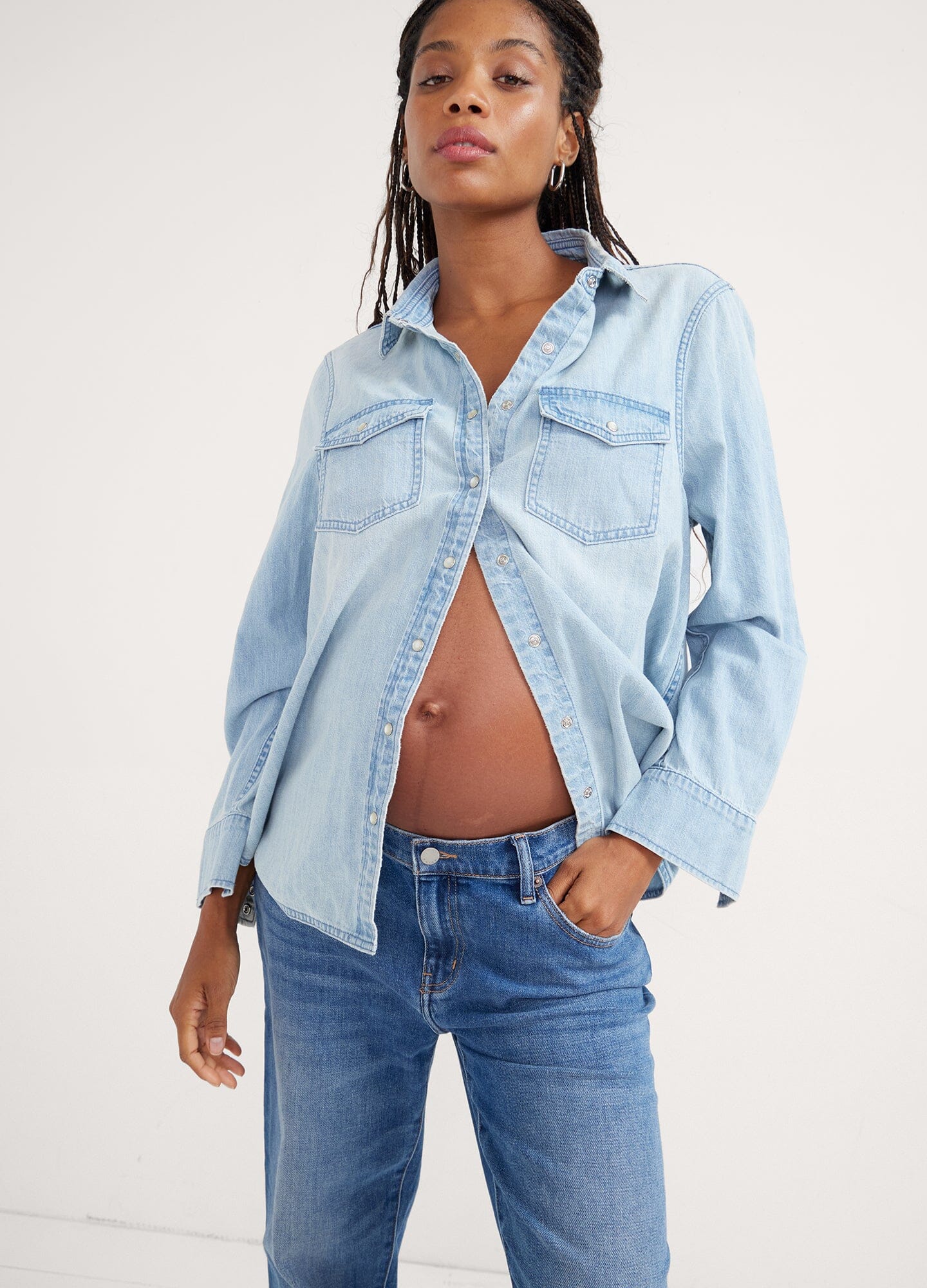 The Denim Maternity Shirt - Light wash denim maternity shirt with rolled sleeves, worn open over a white tank top during pregnancy.
