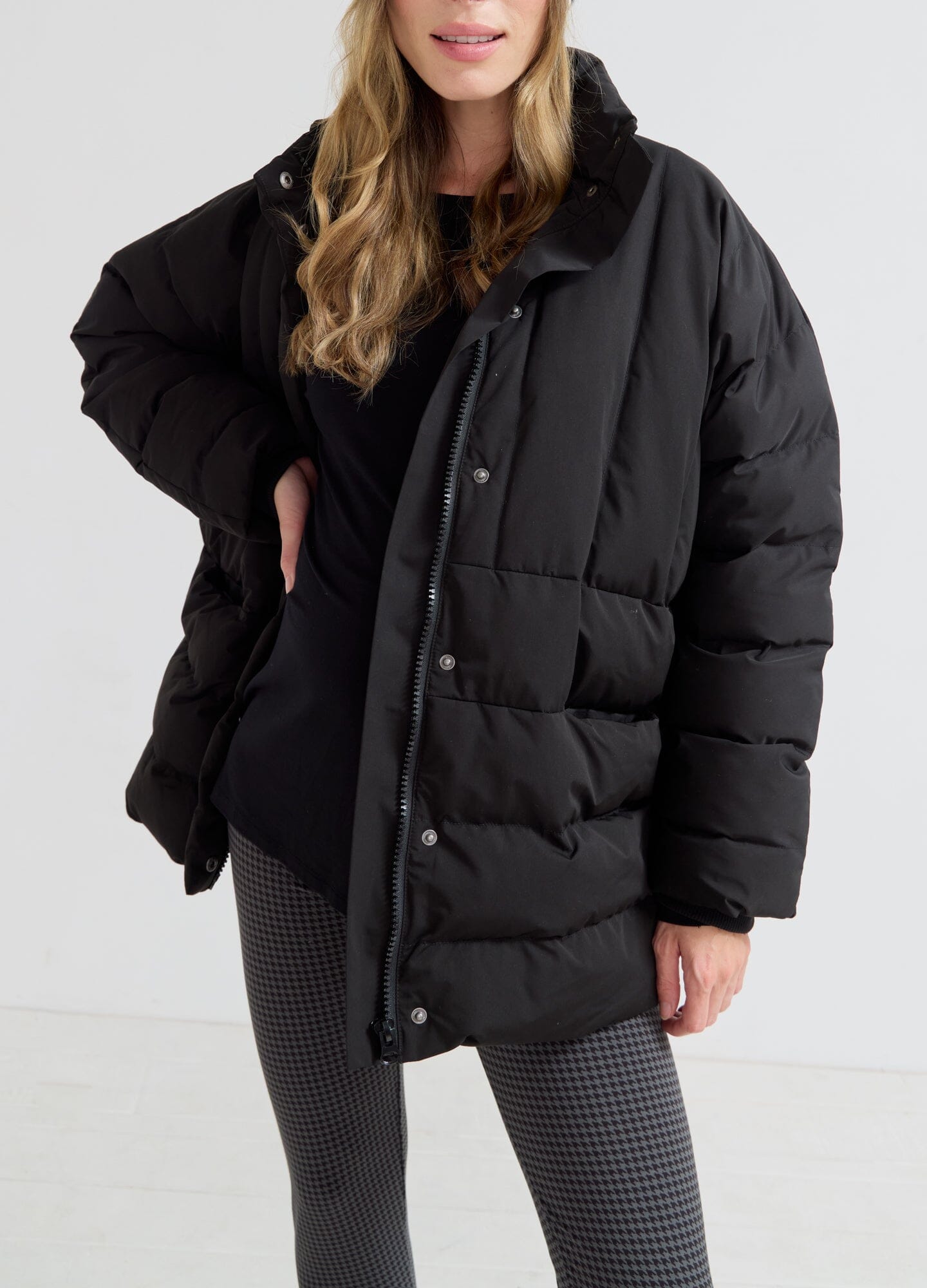 The Mother Puffer - Black puffer jacket styled with maternity top and gray leggings, ideal for pregnancy and postpartum layering.