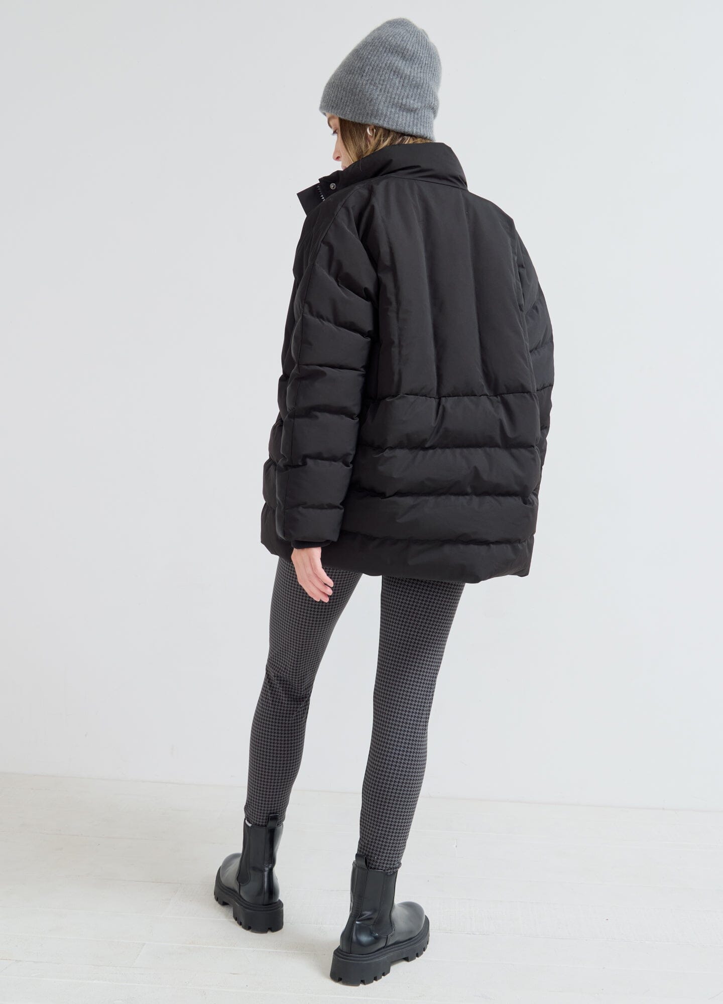 The Mother Puffer - Black puffer jacket styled with maternity top and gray leggings, ideal for pregnancy and postpartum layering.