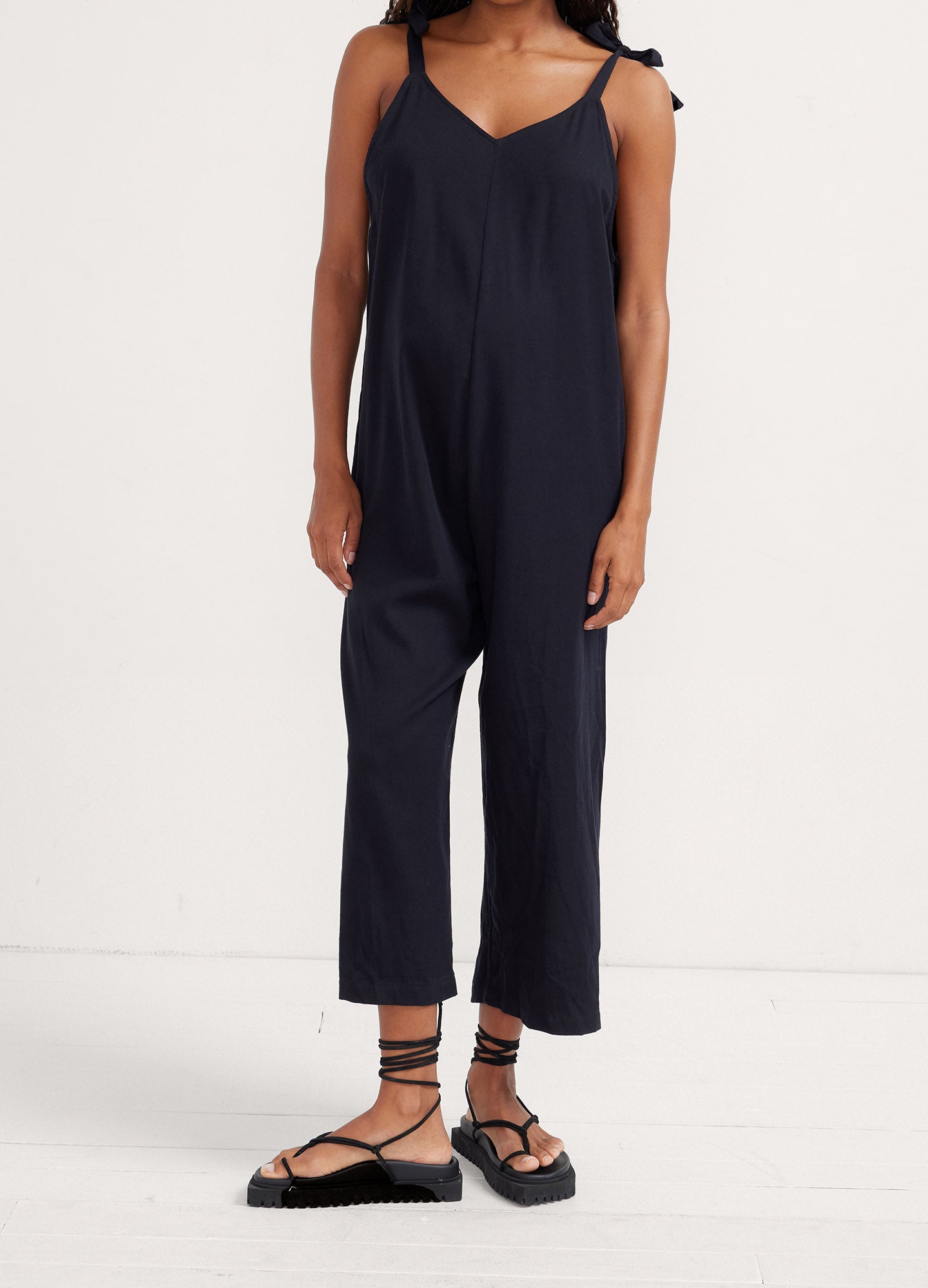 Navy blue maternity jumpsuit with adjustable shoulder ties, loose fit, cropped legs.