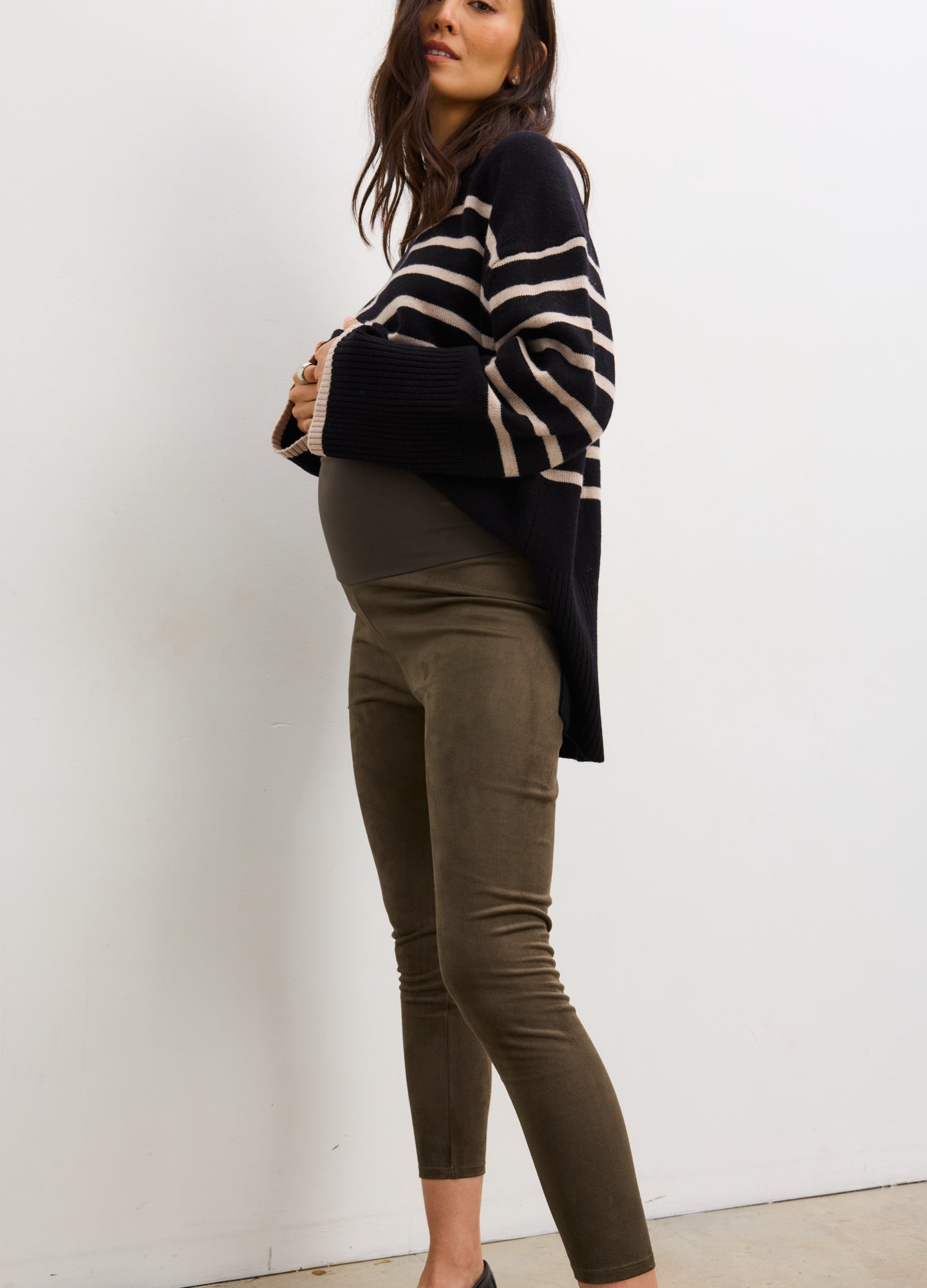 Pregnant woman wearing a navy and beige striped sweater and green pants against a white background