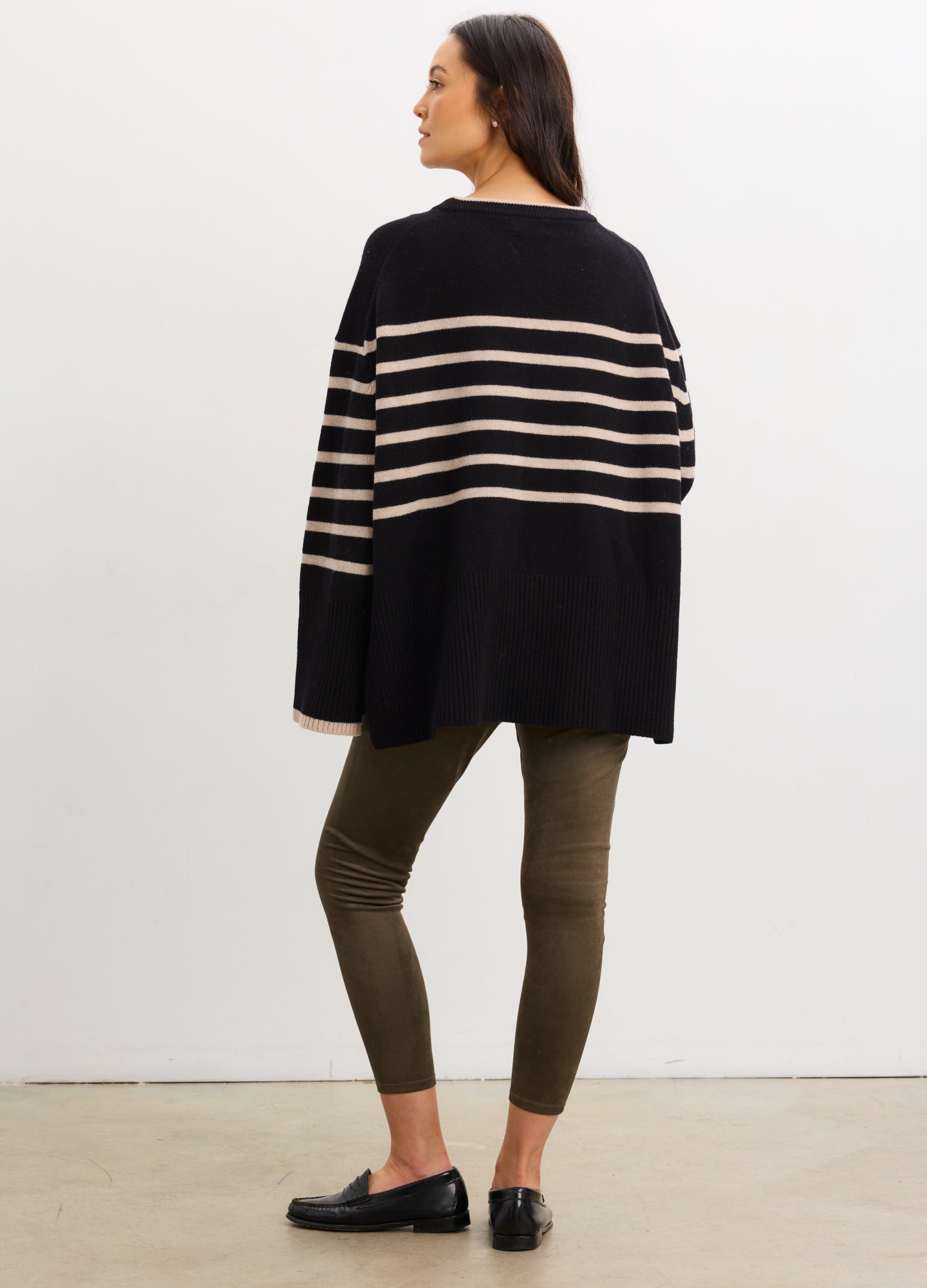 Pregnant woman wearing a navy and beige striped sweater and green pants against a white background