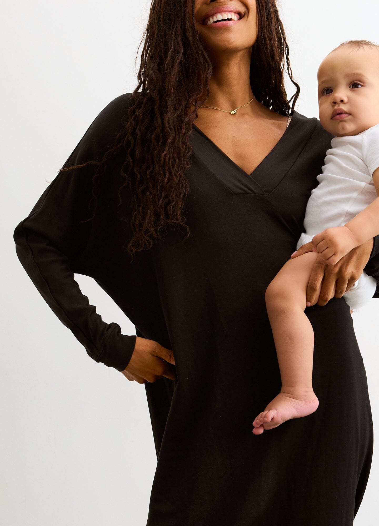 The Visitor Dress - Black maternity dress with long sleeves and V-neck, designed for pregnancy, nursing, and postpartum, modeled with baby.