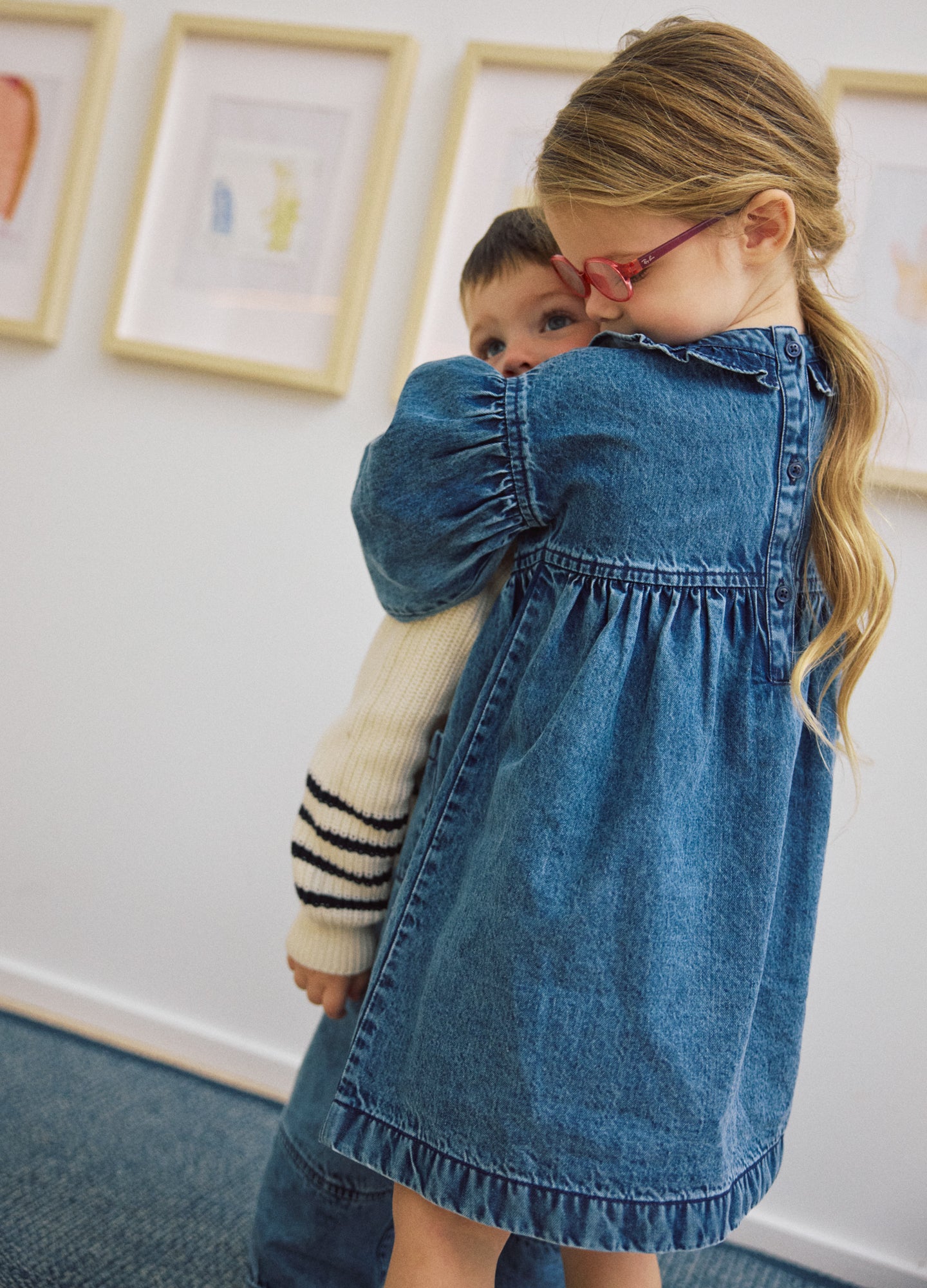 Blue denim maternity dress with long puffed sleeves and gathered waist, worn by a child holding a baby.