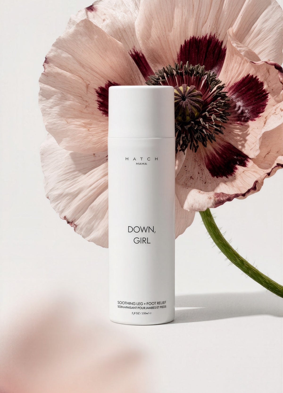 Tall white cylindrical skincare bottle labeled Down, Girl with a large pale pink and burgundy flower backdrop.