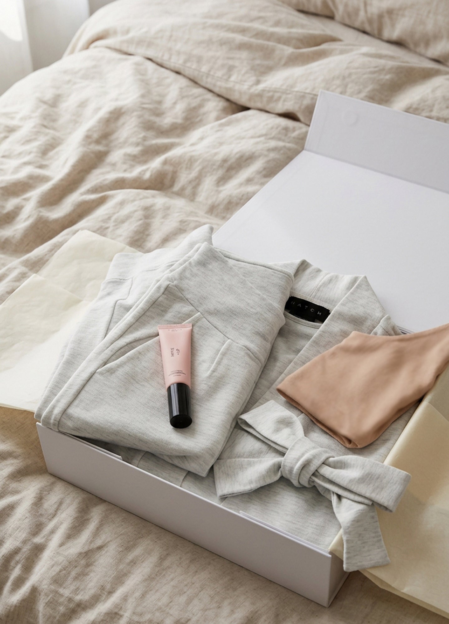 Nude and pink nursing robe and cloth bundle with soft fabric face mask and pink tube of cream in white gift box.