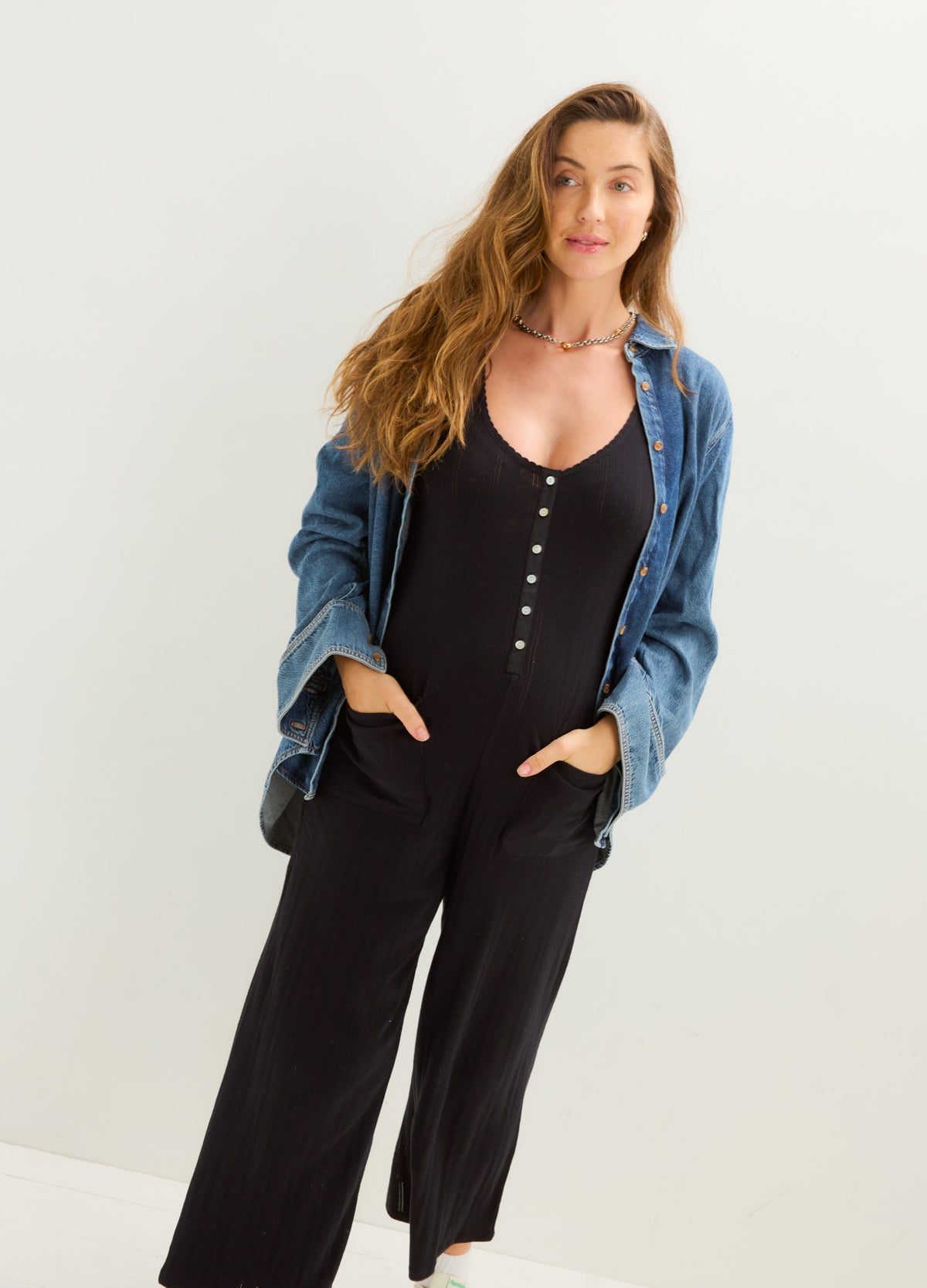 Black sleeveless maternity jumpsuit with scoop neck, button front, wide legs, and side pockets, styled with a blue denim.