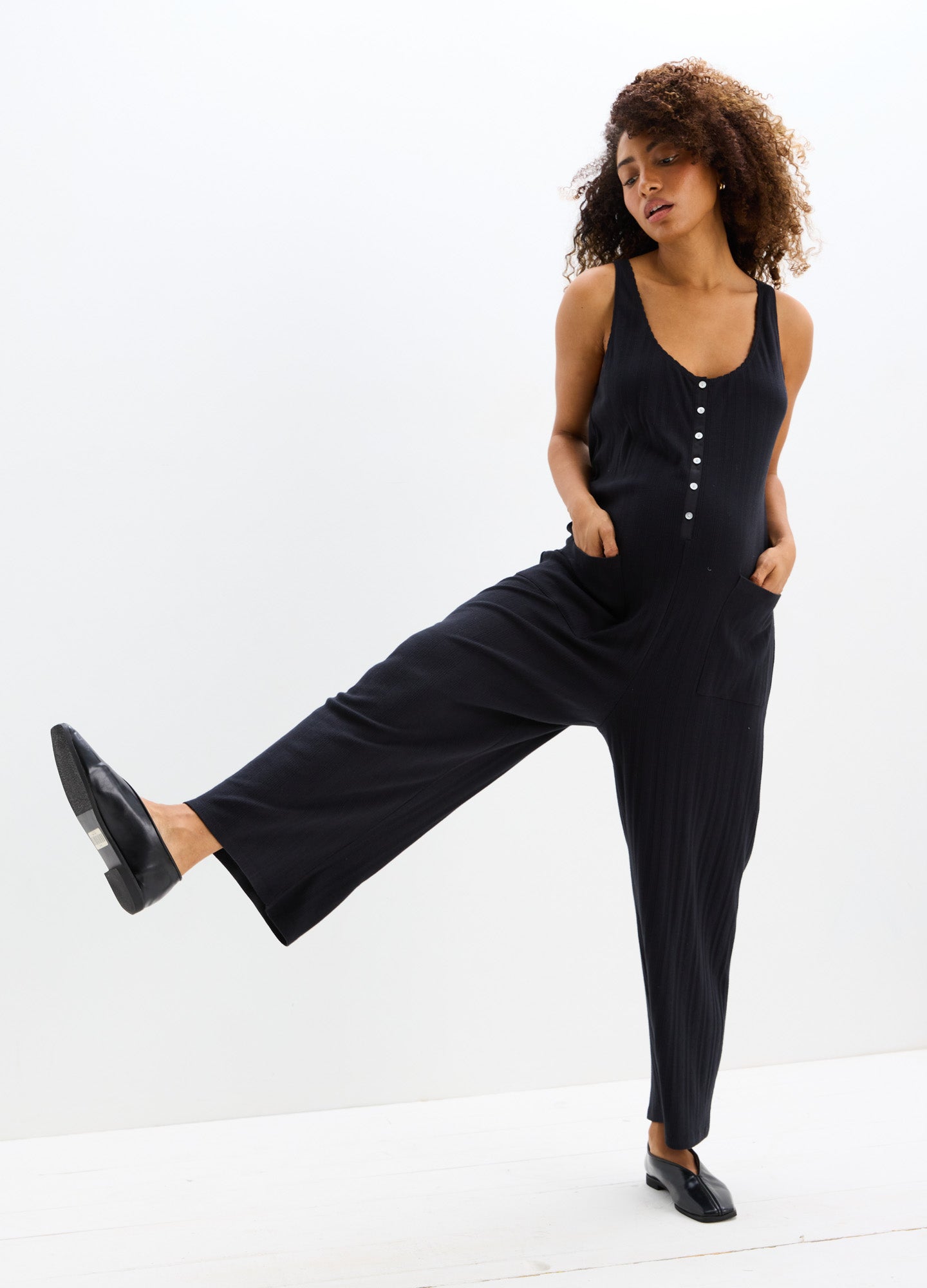 Black sleeveless maternity jumpsuit with button front, scoop neckline, and wide-leg pants.