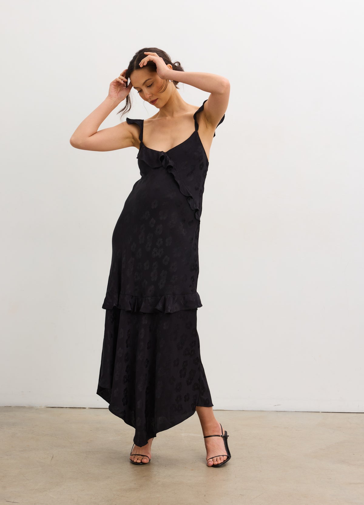 Black jacquard maternity slip dress with bias cut, tiered hem, and thin adjustable straps.