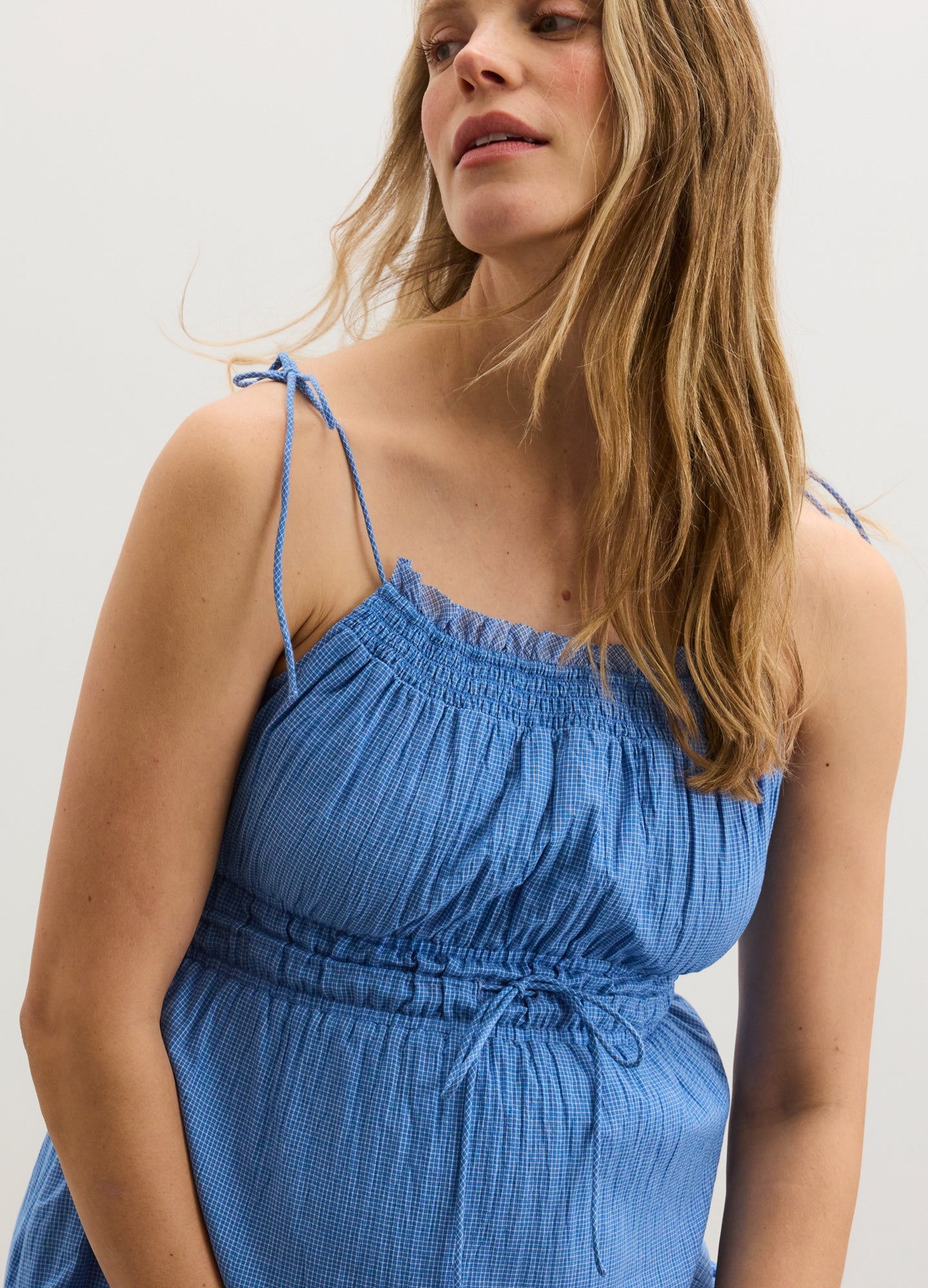 Light blue sleeveless maternity dress with adjustable tie straps and ruched bodice detailing.