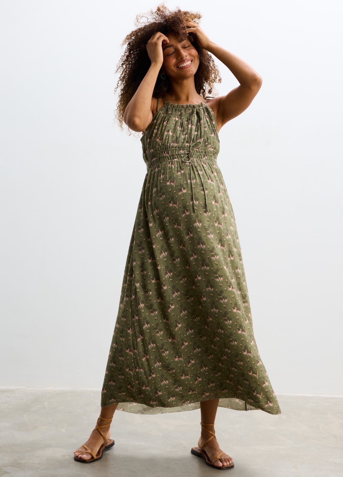 Olive green maternity maxi dress with small floral print, sleeveless with adjustable tie straps and loose, flowing skirt.