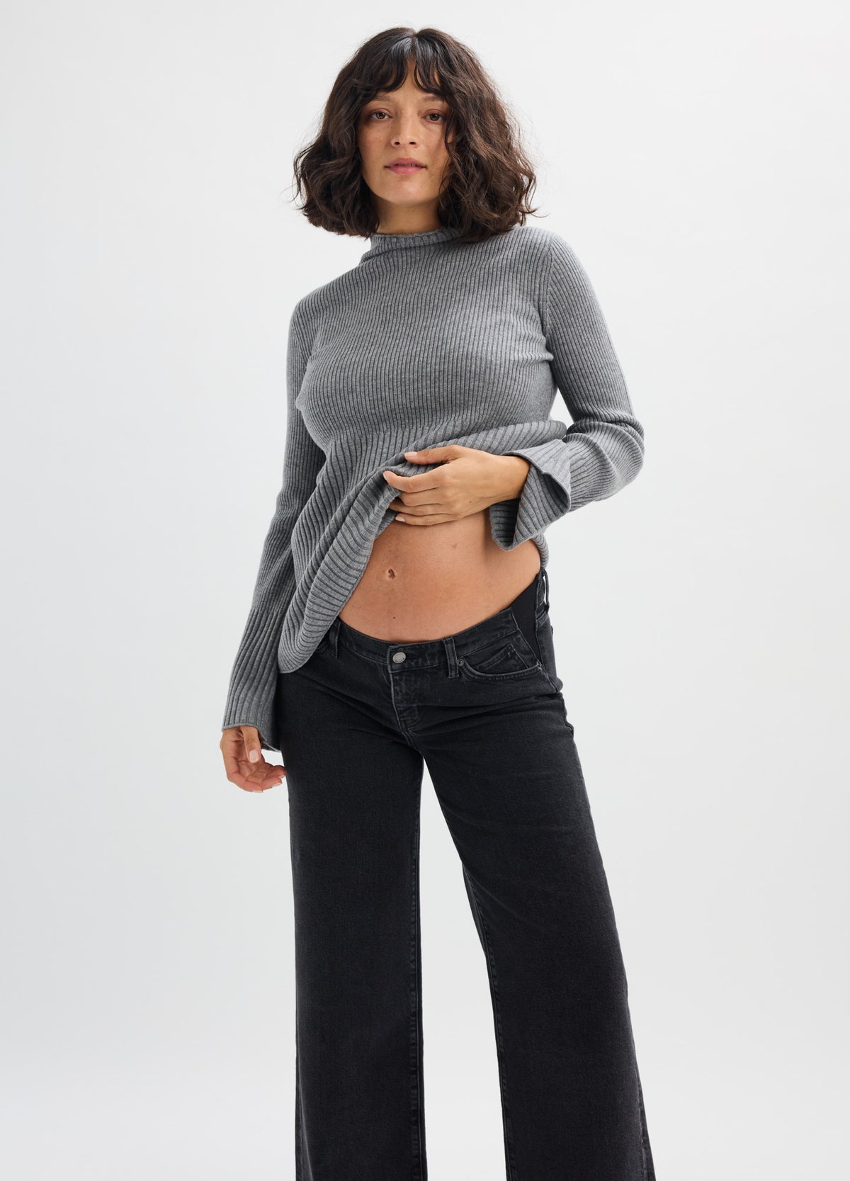 Light grey, fitted knit turtleneck sweater styled for maternity, paired with black pants on pregnant model.