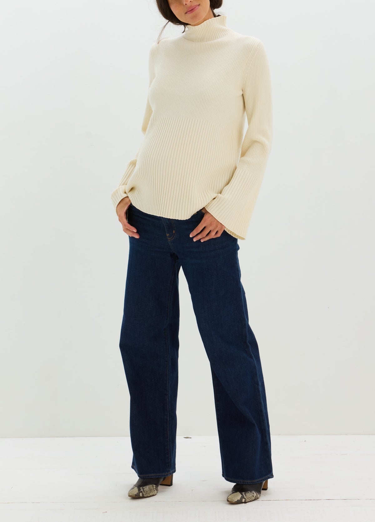 Cream-colored ribbed maternity turtleneck sweater with long sleeves, worn over dark wide-leg jeans.