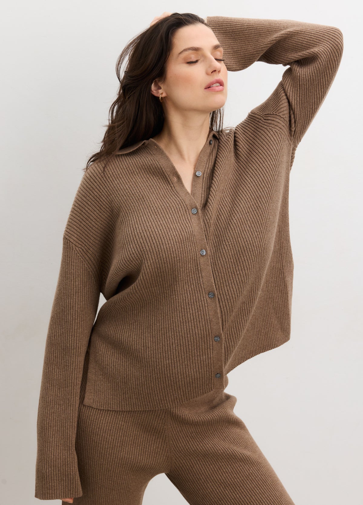 Pregnant woman wearing brown ribbed knit buttondown maternity polo with long sleeves and relaxed fit.