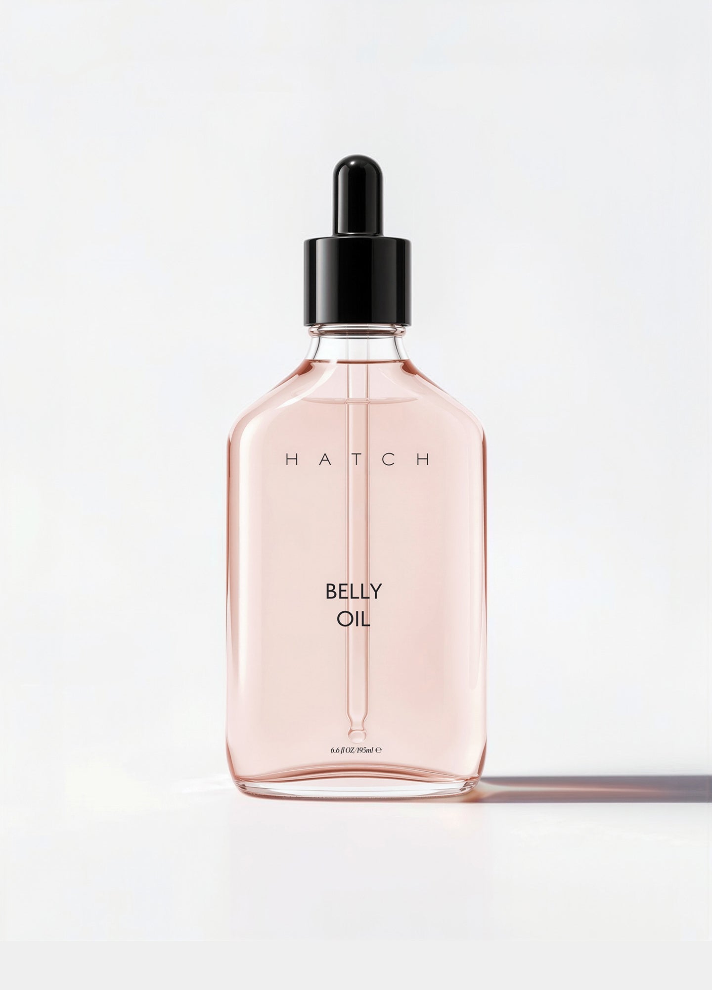Clear rectangular glass bottle with pale pink belly oil and black dropper cap, labeled Hatch Belly Oil.