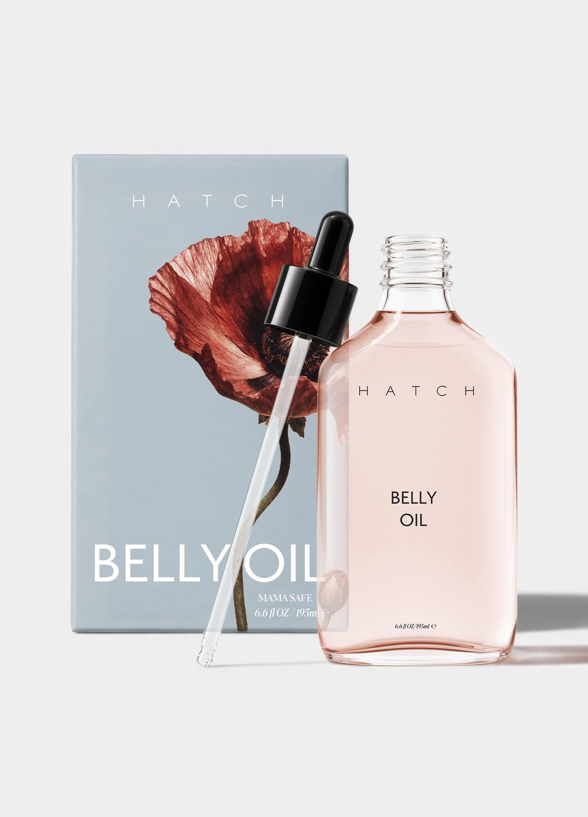 Clear rectangular bottle of light pink belly oil with black dropper, next to blue box featuring red floral illustration and.