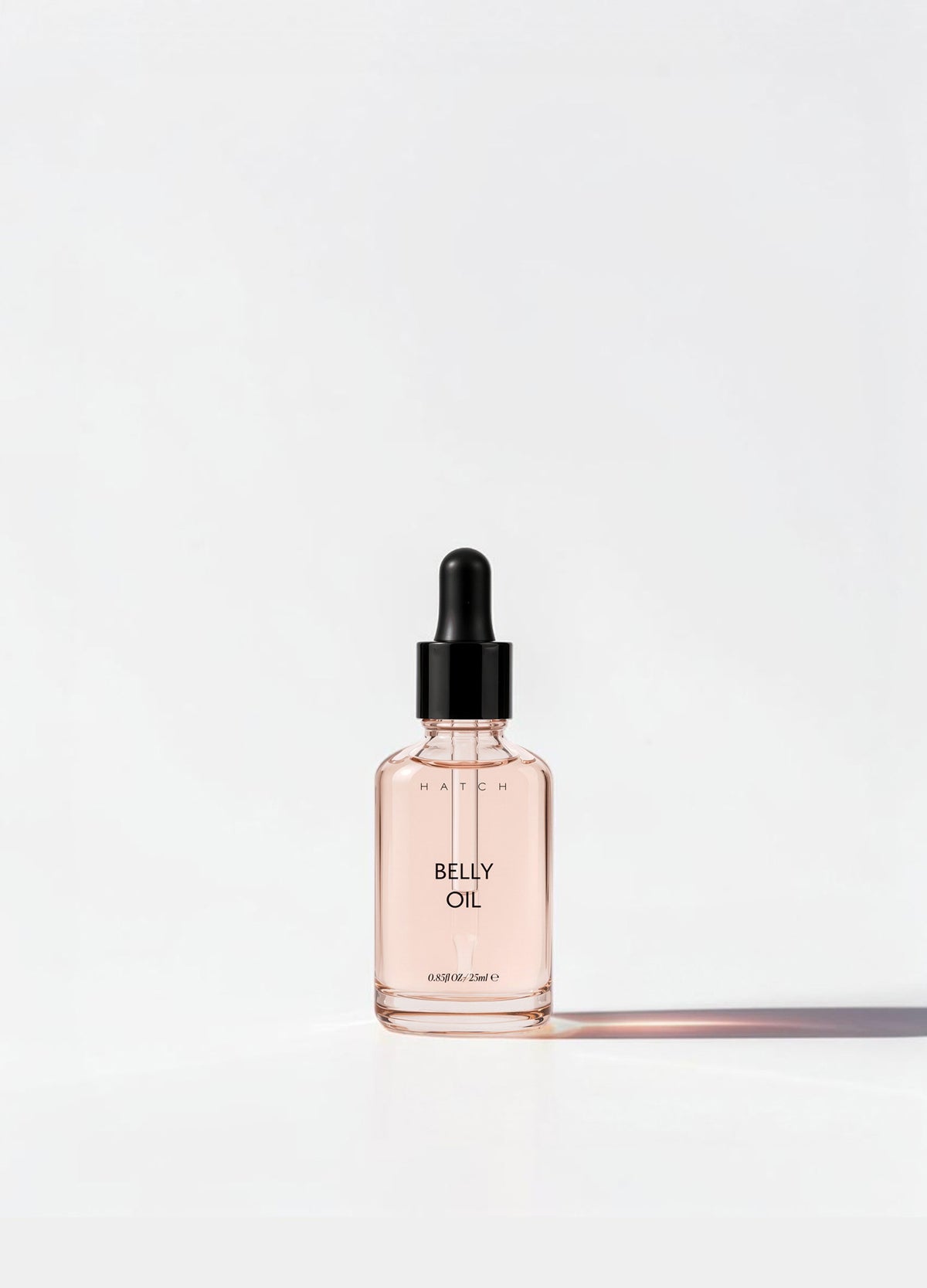 Clear small glass bottle with pale pink belly oil and black dropper cap, elegant and minimalistic design.