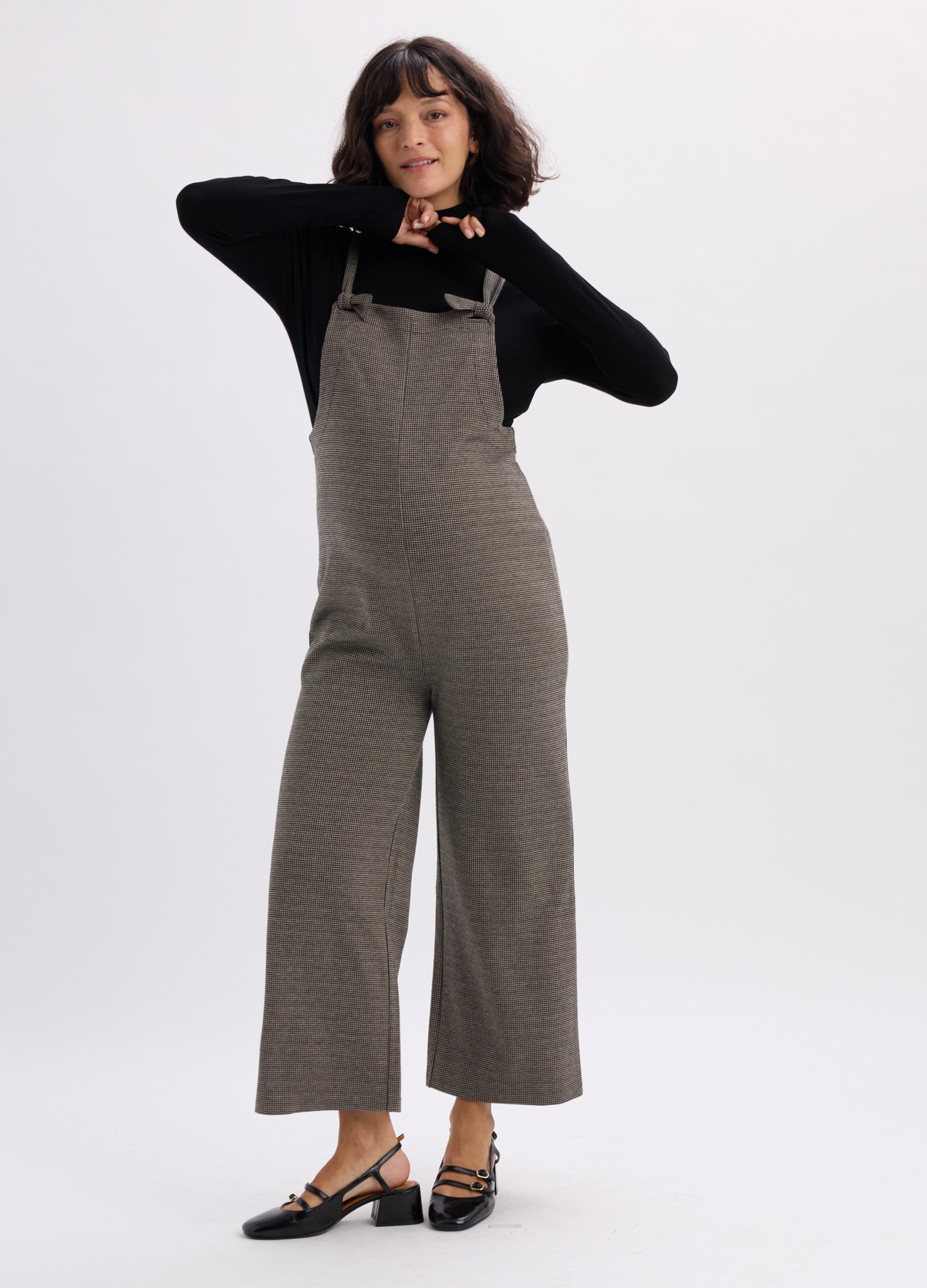 Olive green maternity onesie with wide legs and adjustable shoulder straps worn over black long-sleeve top.