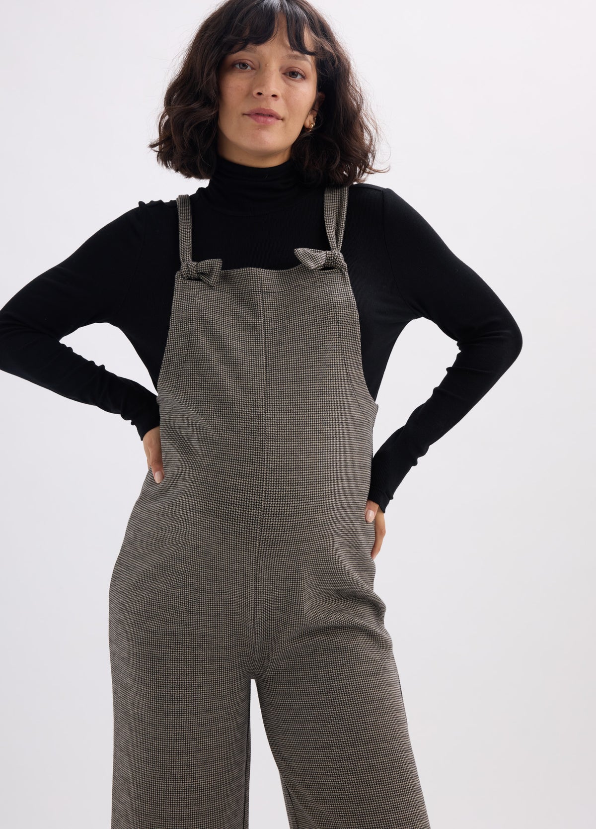 Olive green maternity onesie with adjustable shoulder straps and loose-fit pant legs over black long-sleeve turtleneck.