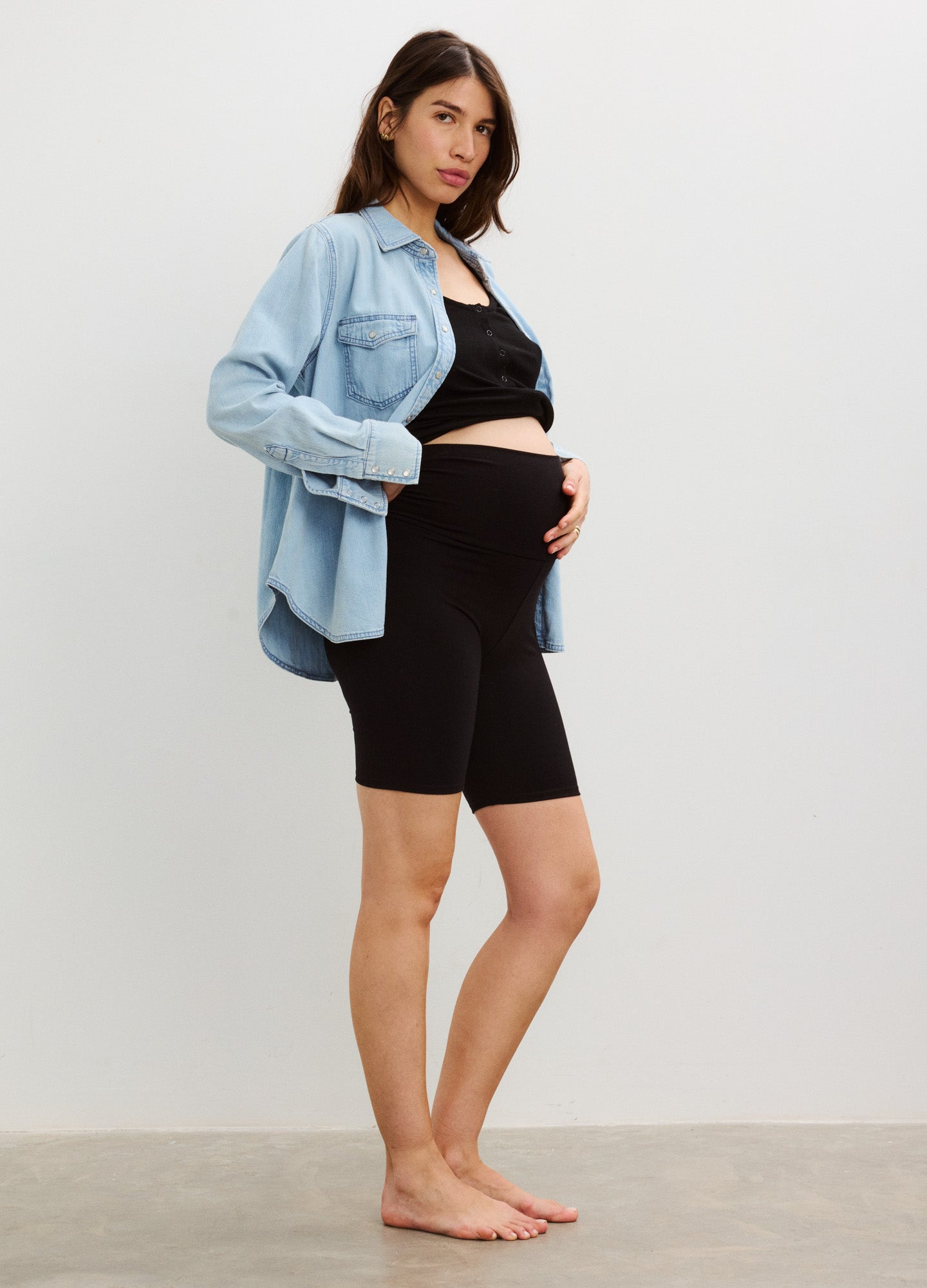 Black high-waist maternity bike shorts with stretchy fabric, paired with a loose light blue shirt and black crop top.