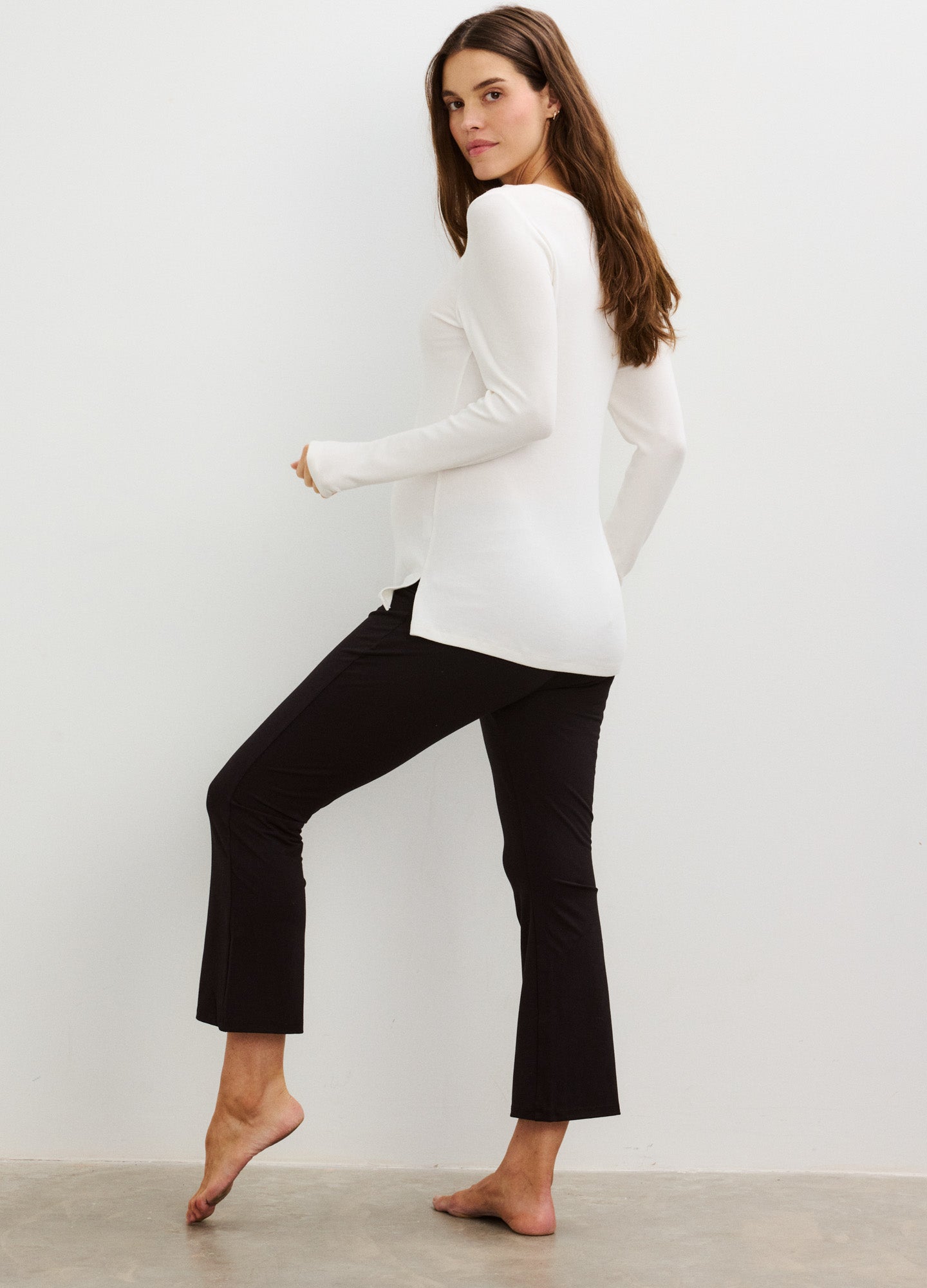 Black maternity crop flare leggings styled with a fitted white long-sleeve top, designed for pregnancy comfort and stretch.