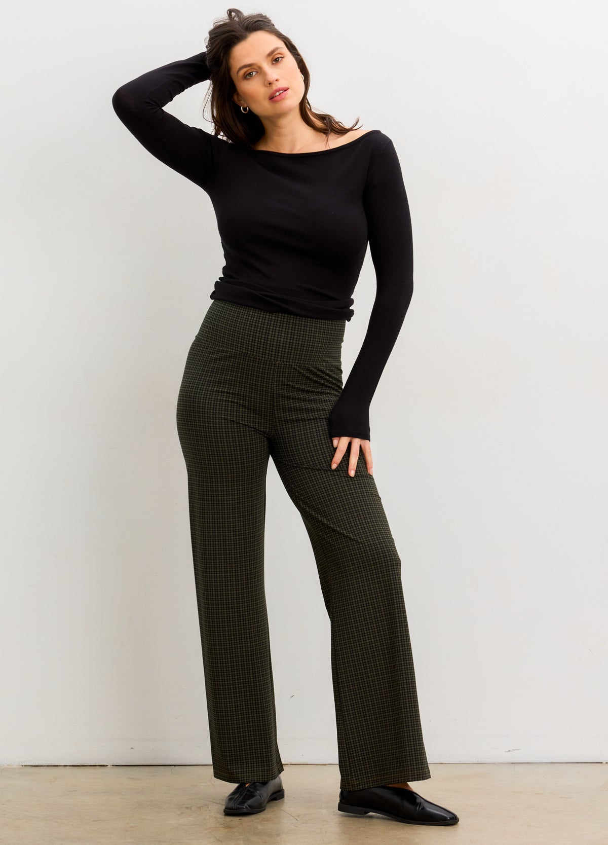 Pregnant woman wearing a black top and plaid pants sitting on a white background