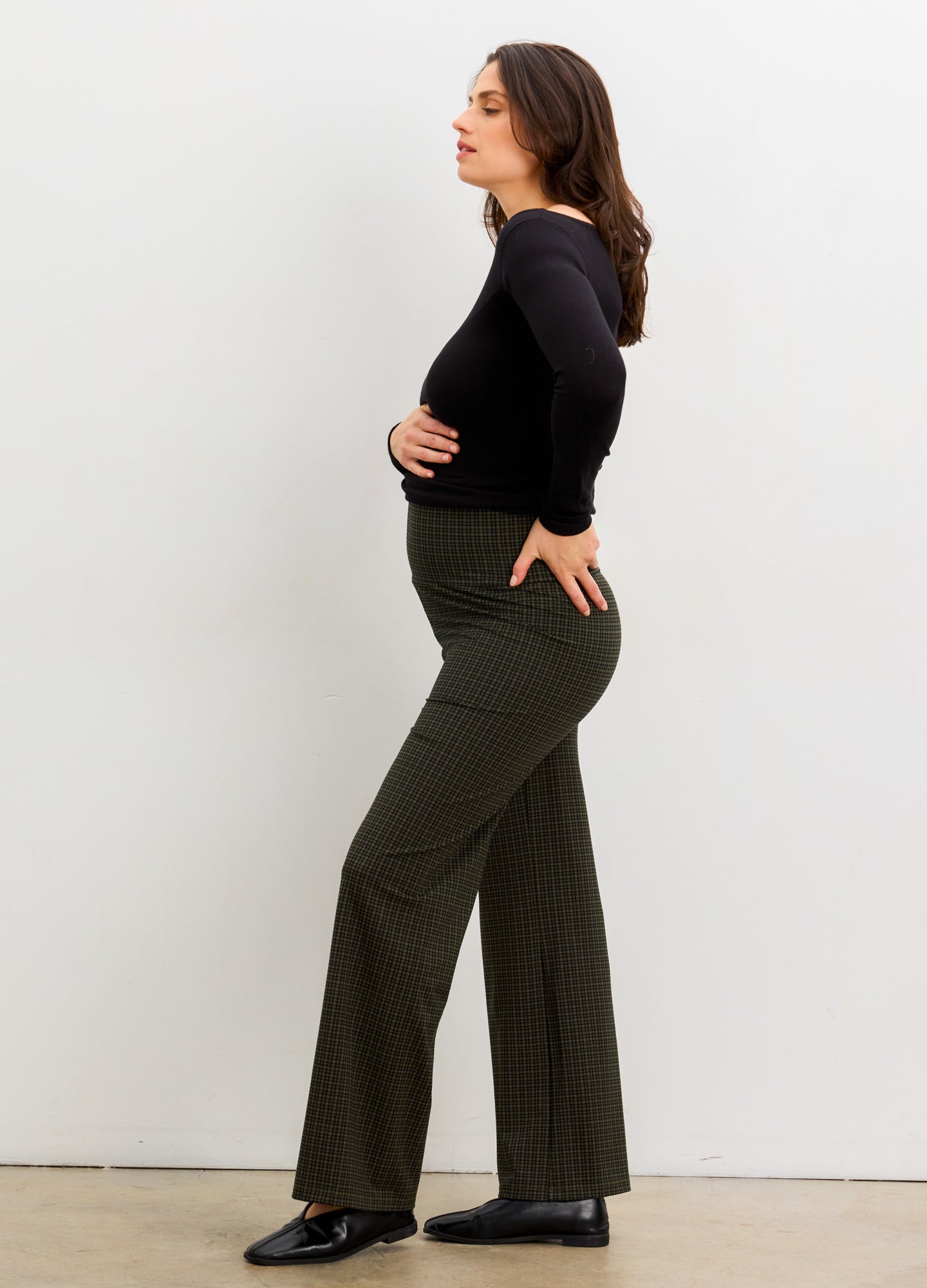 Pregnant woman wearing a black top and green checkered pants against a white background