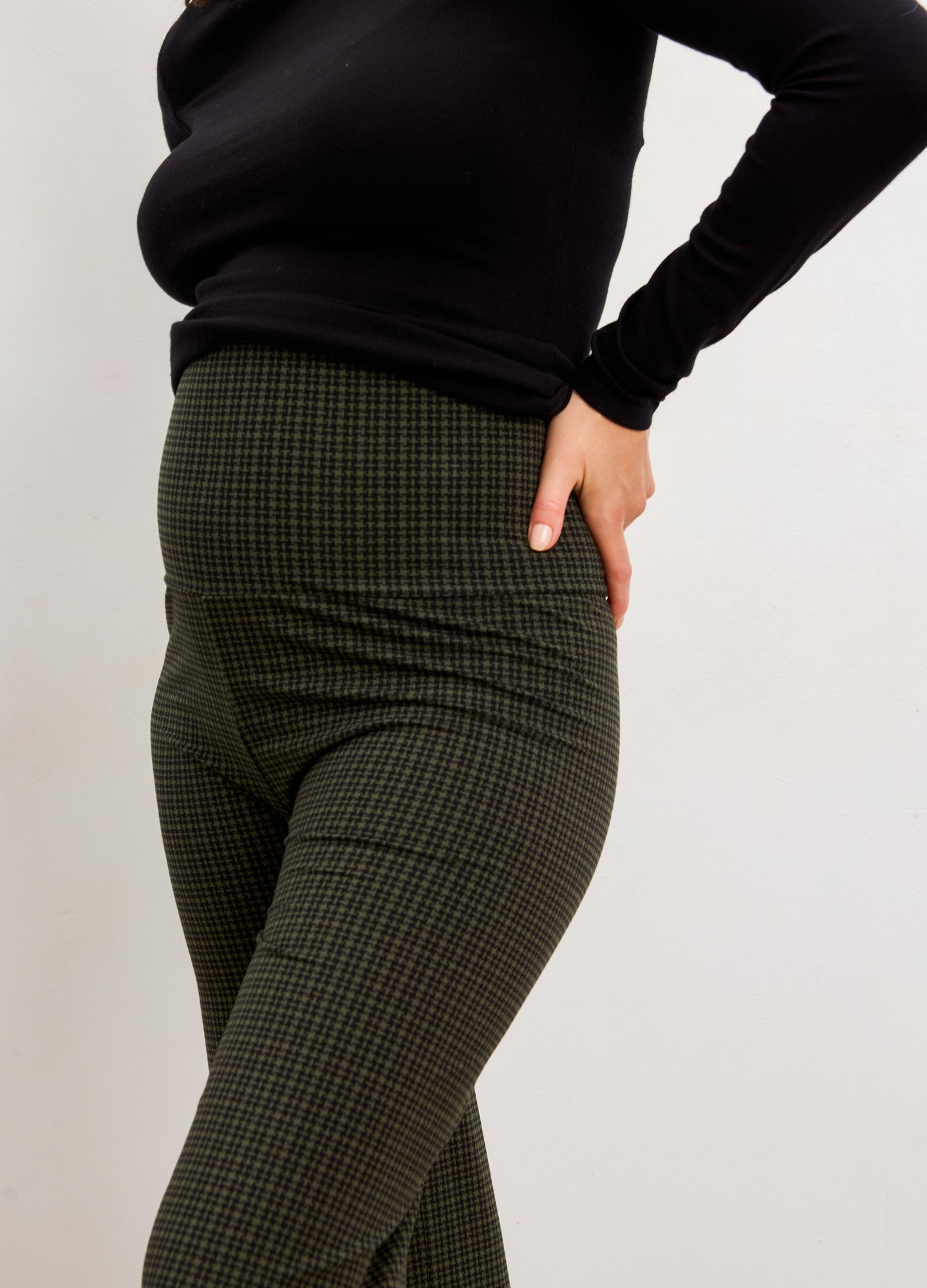 Pregnant woman wearing a black top and green checkered pants against a white background