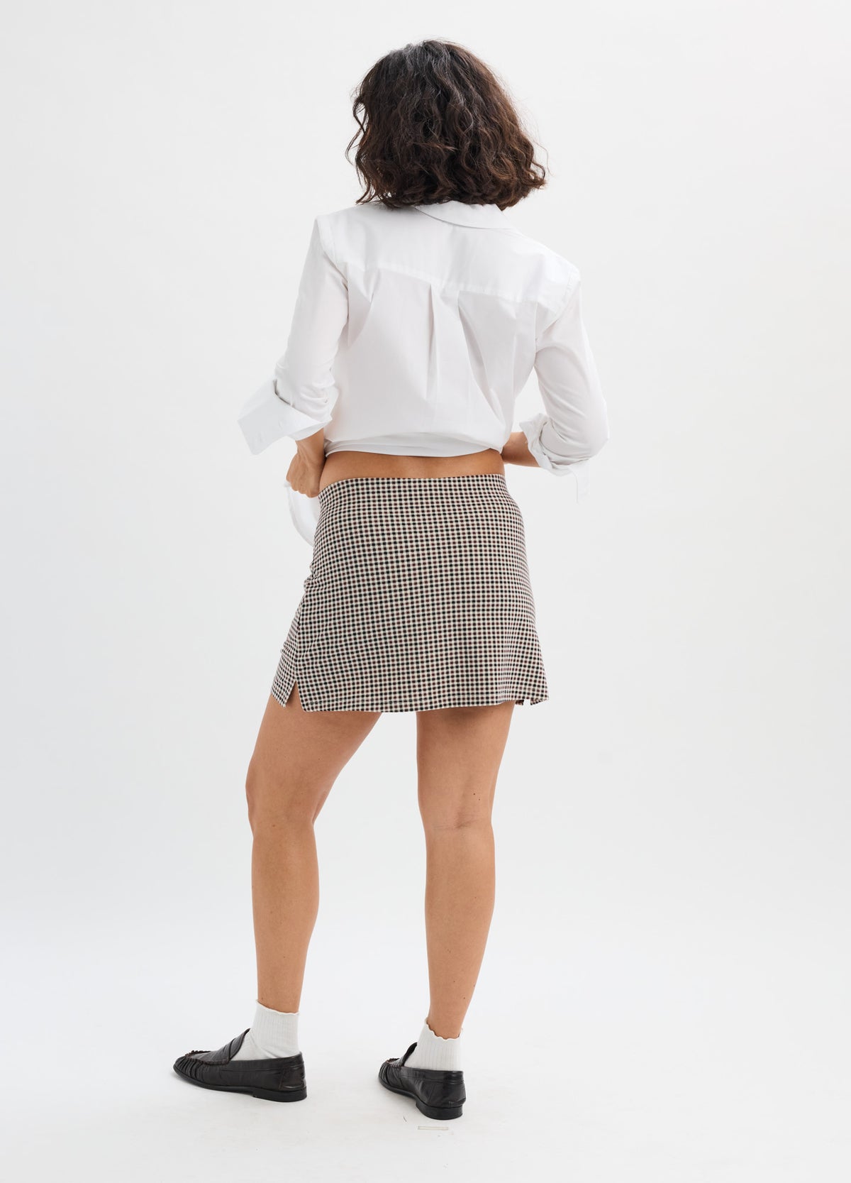 Pregnant woman wearing a gray checkered maternity skort with a high waistband and white blouse.