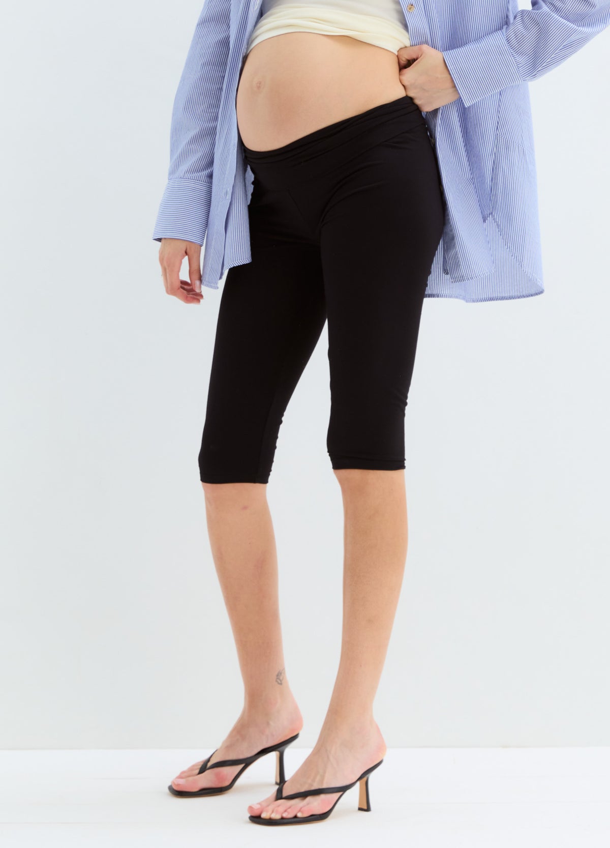 Black knee-length maternity capri leggings with a supportive high waistband, worn with a light blue shirt and beige top.