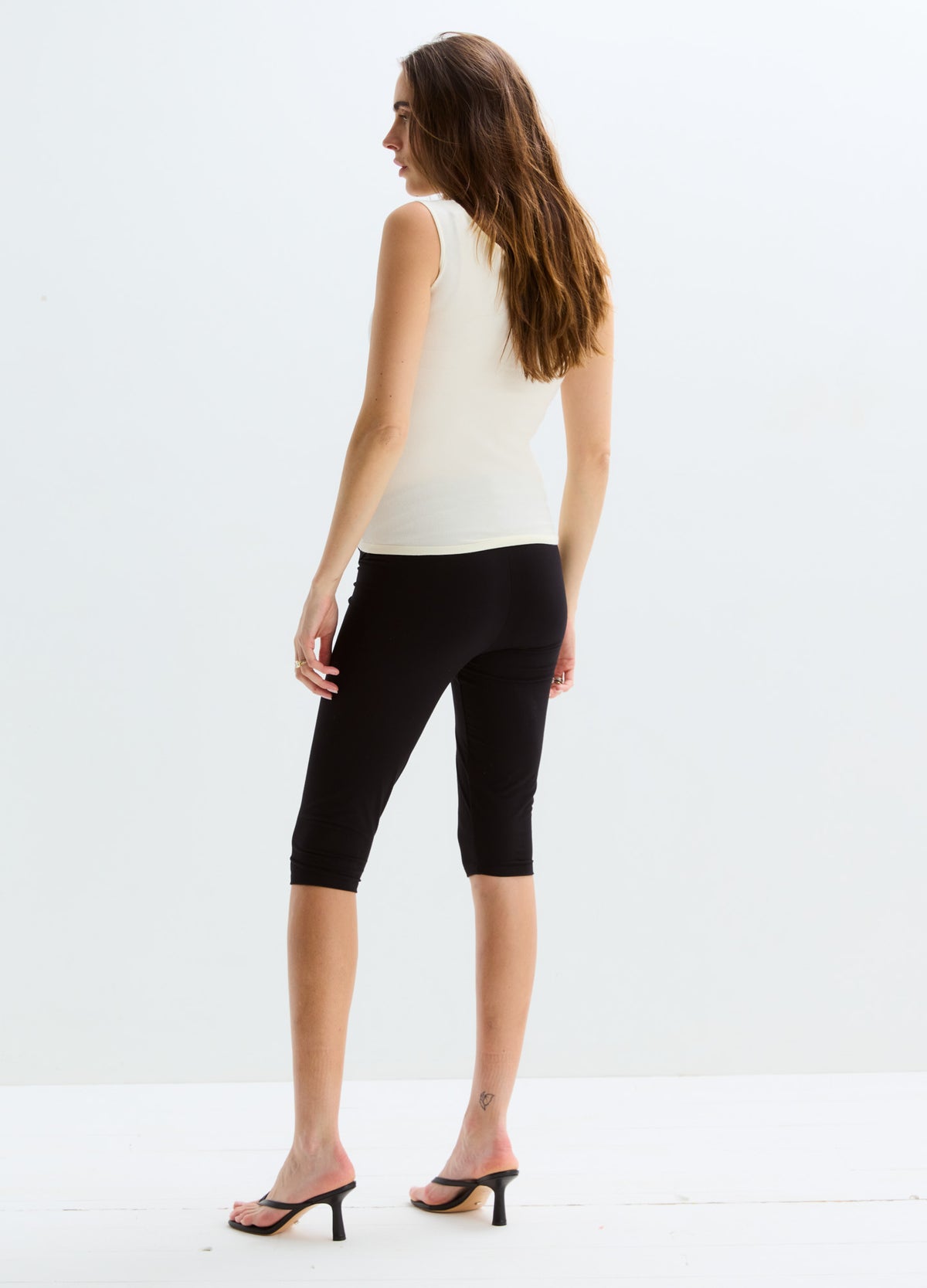 Black cropped maternity leggings with a high, stretchy waistband paired with a sleeveless white top and black heeled sandals.