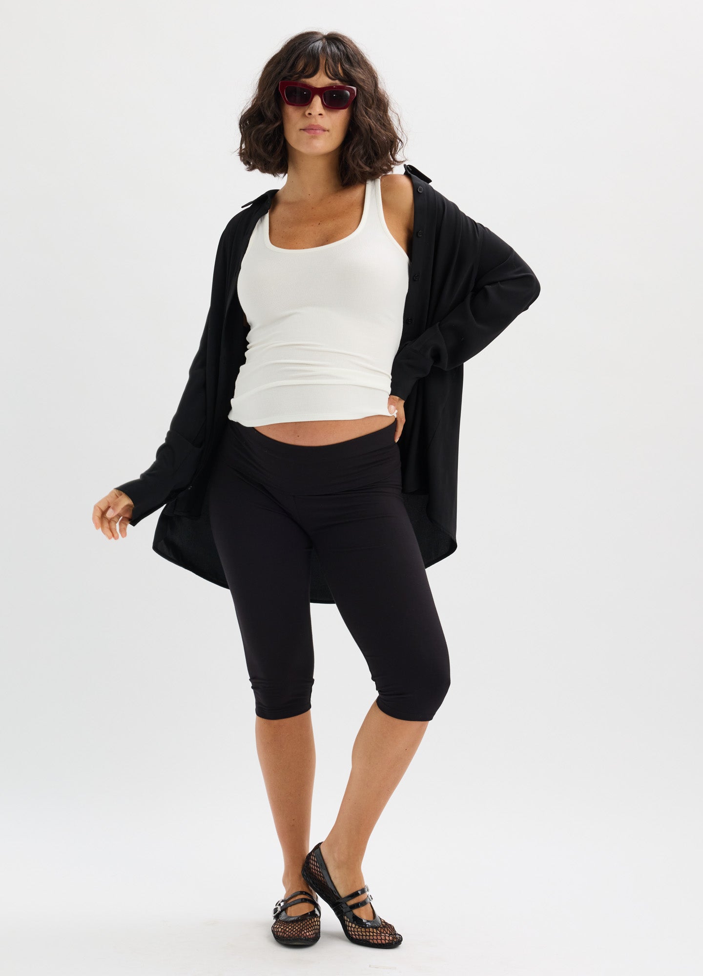 Black mid-calf maternity leggings with high stretch fit, paired with white tank and loose black cardigan.