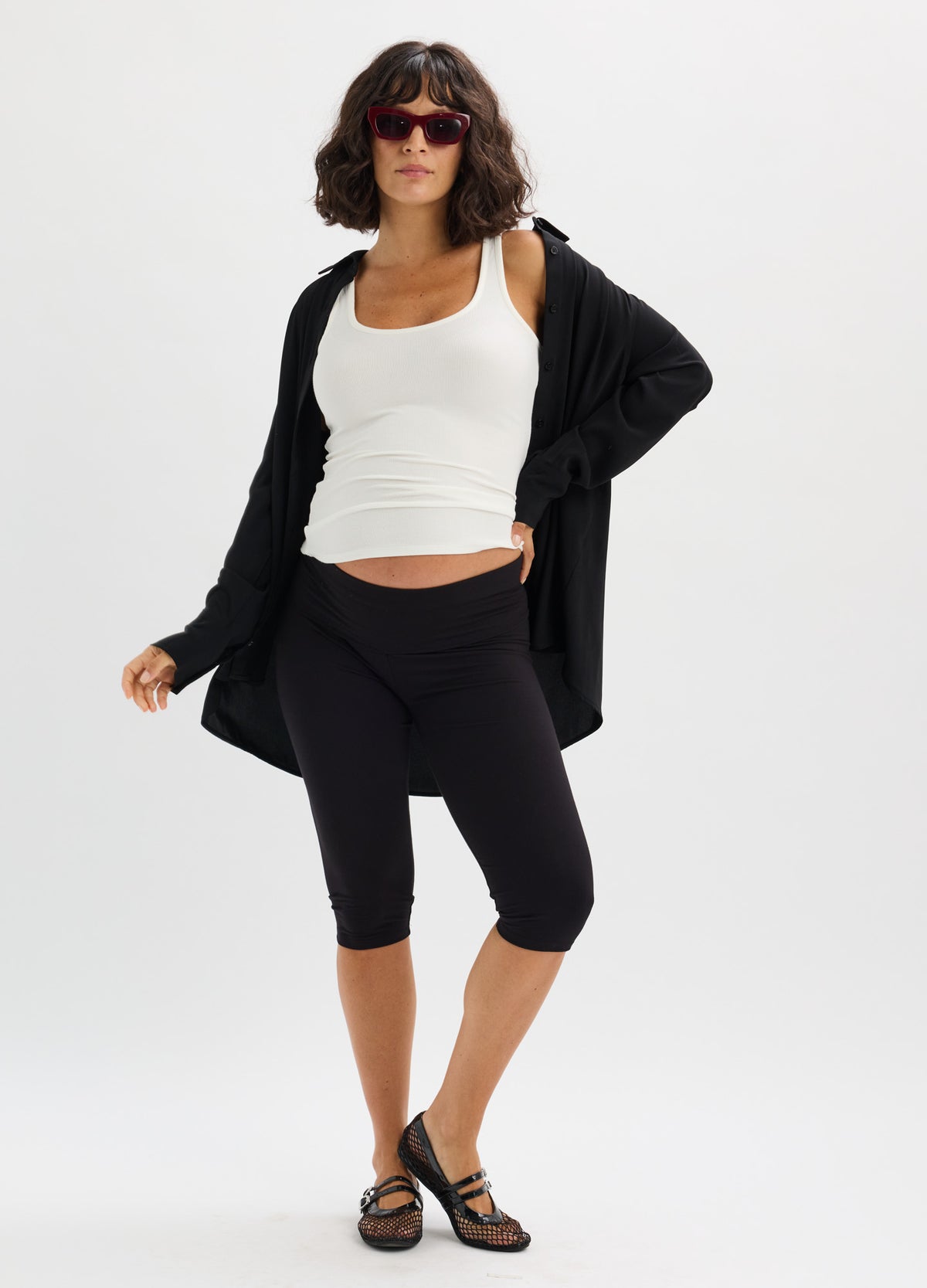 Black mid-calf maternity leggings with high stretch fit, paired with white tank and loose black cardigan.