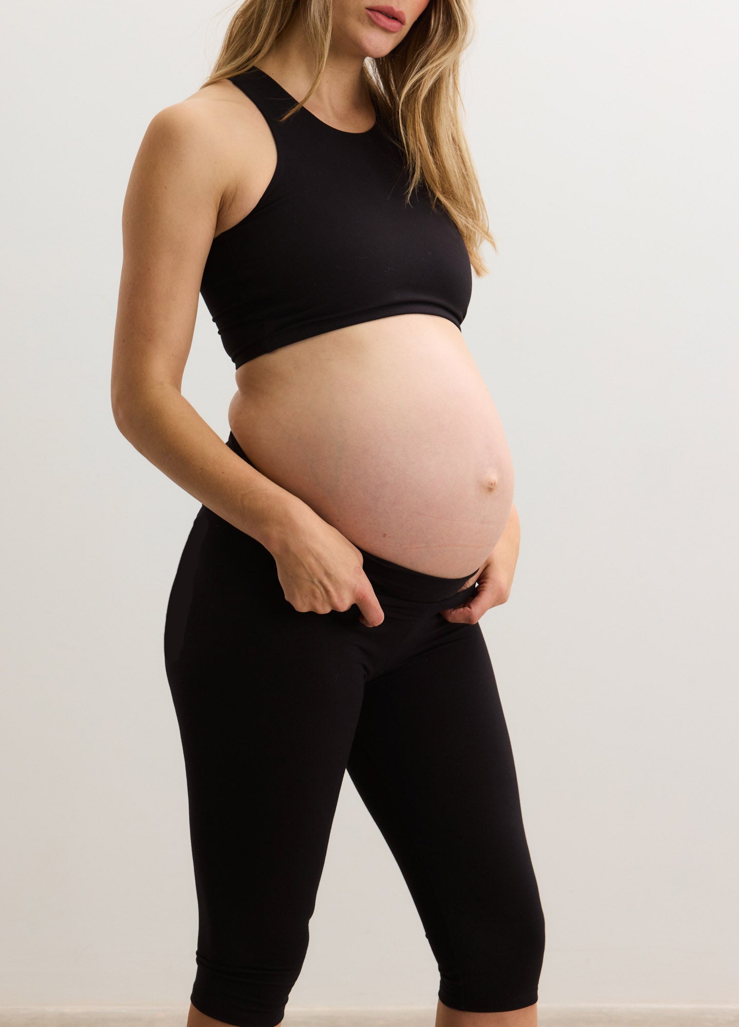 Black capri maternity leggings with high stretch waist, fitted on pregnant woman.