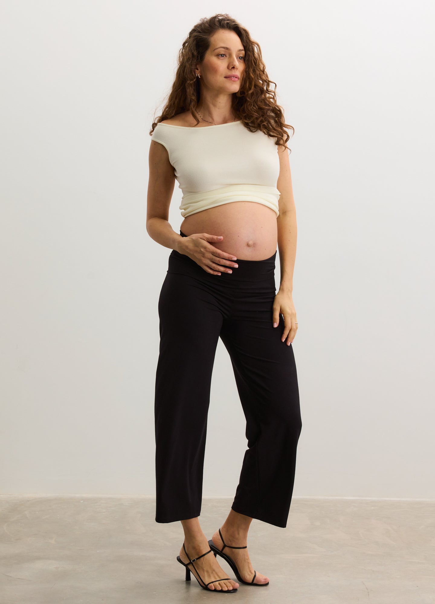Black maternity crop pants with elastic waistband, straight leg fit, worn by pregnant model paired with cream cropped top.