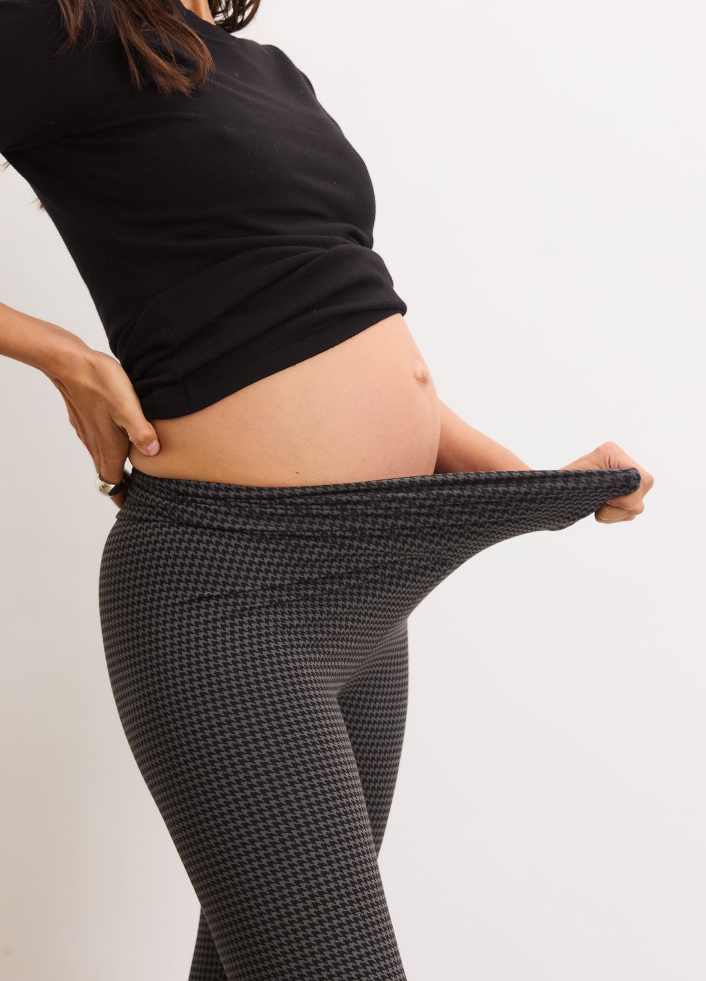 Black and white houndstooth maternity leggings with a stretchy waistband worn over pregnant belly.