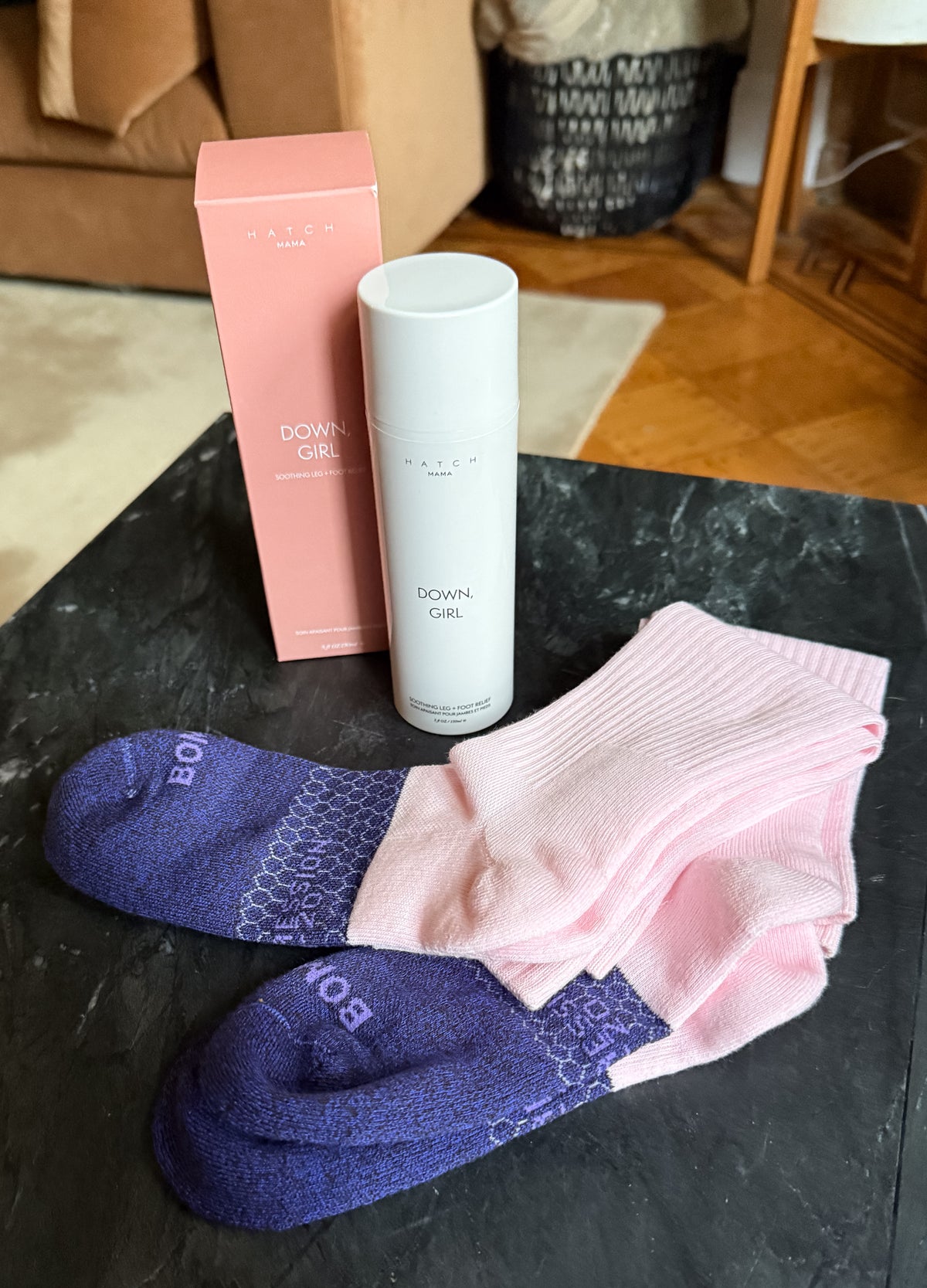 Pink maternity compression socks with purple foot grips next to white skincare spray and a pink box on black surface.