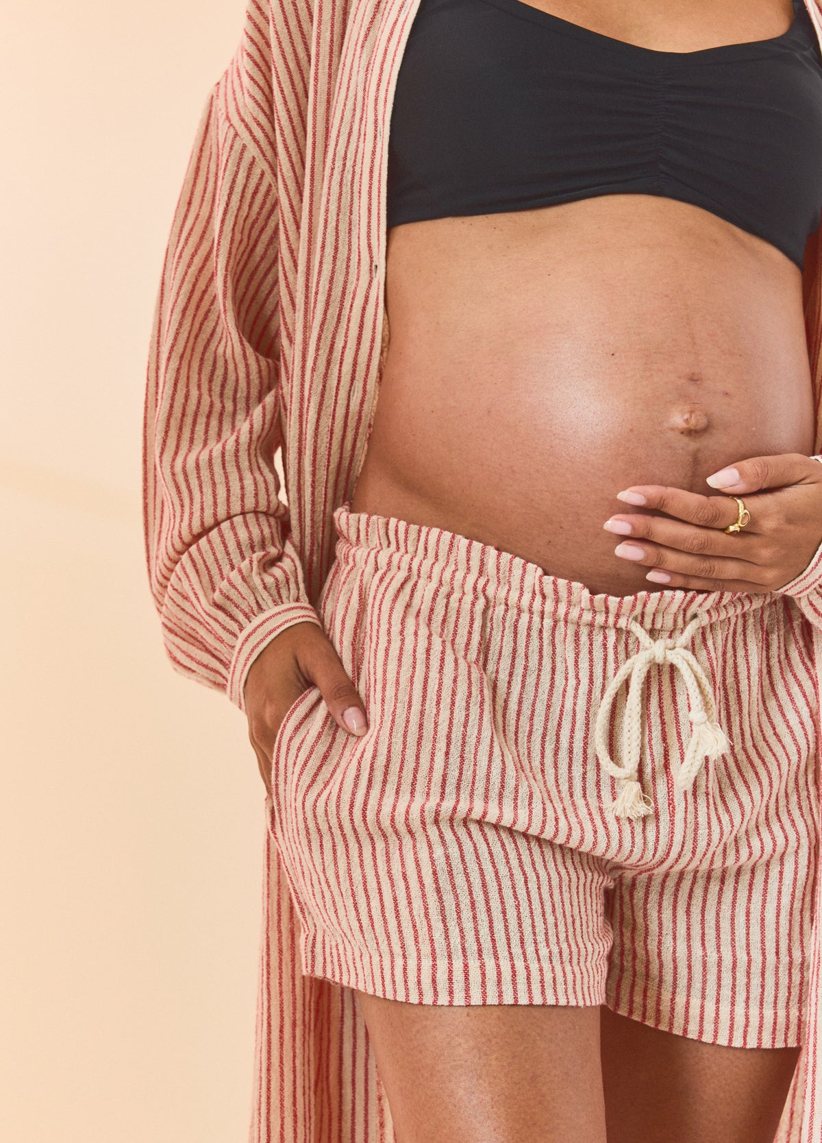 Maternity red and natural striped beach shorts with elastic waistband and drawstring, worn by pregnant model.