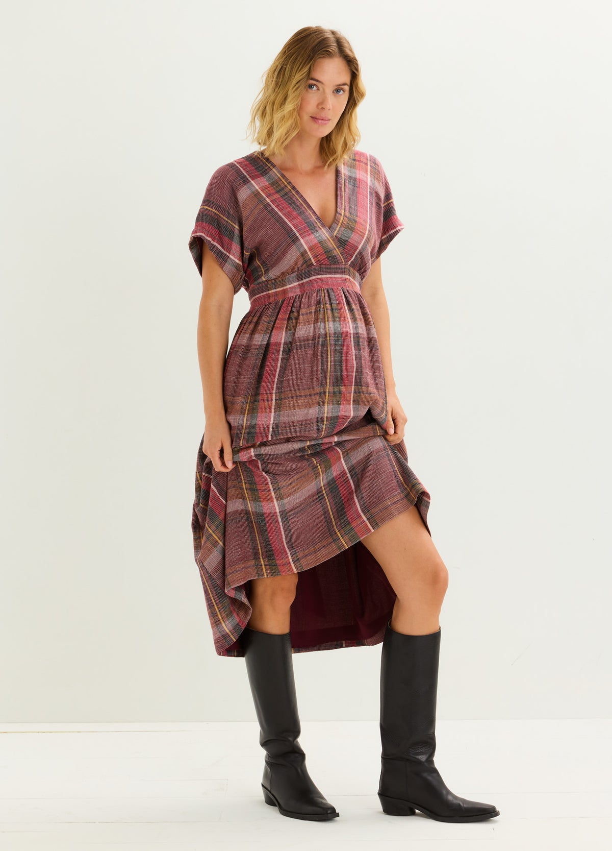 Plaid maternity dress in shades of burgundy and pink with short sleeves and a high-low hemline, paired with black knee-high.