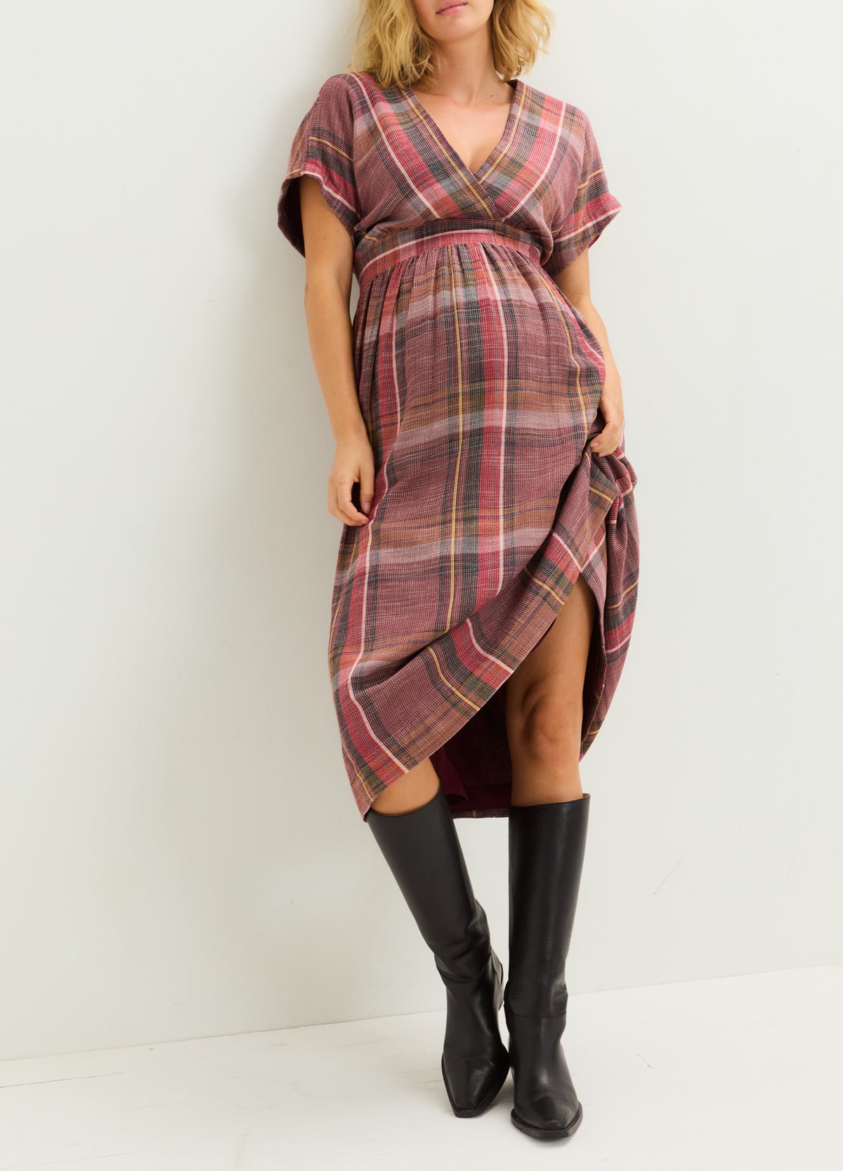 Plaid maternity dress in shades of pink and brown with short sleeves and a wrap v-neck, styled with black knee-high boots.