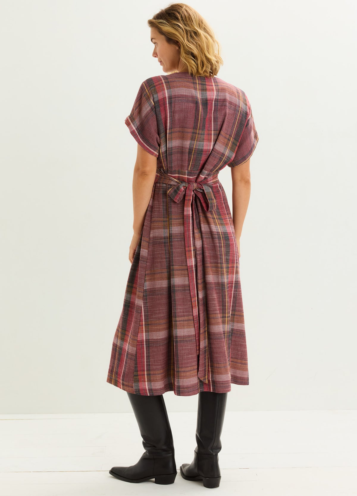 Plaid midi maternity dress with short sleeves and a waist tie in muted red and beige tones paired with black knee-high boots.