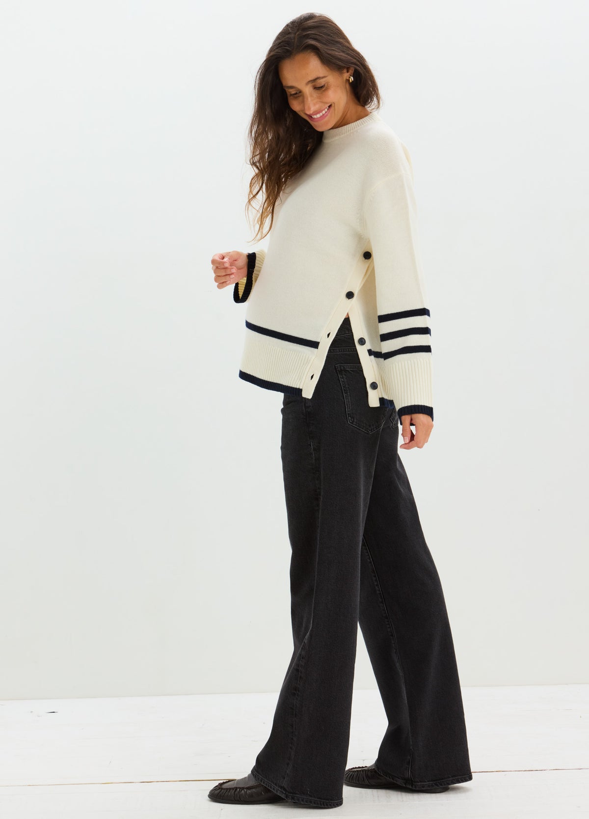 Cream knit maternity sweater with side buttons and navy stripes on sleeves and hem, paired with black wide-leg pants.