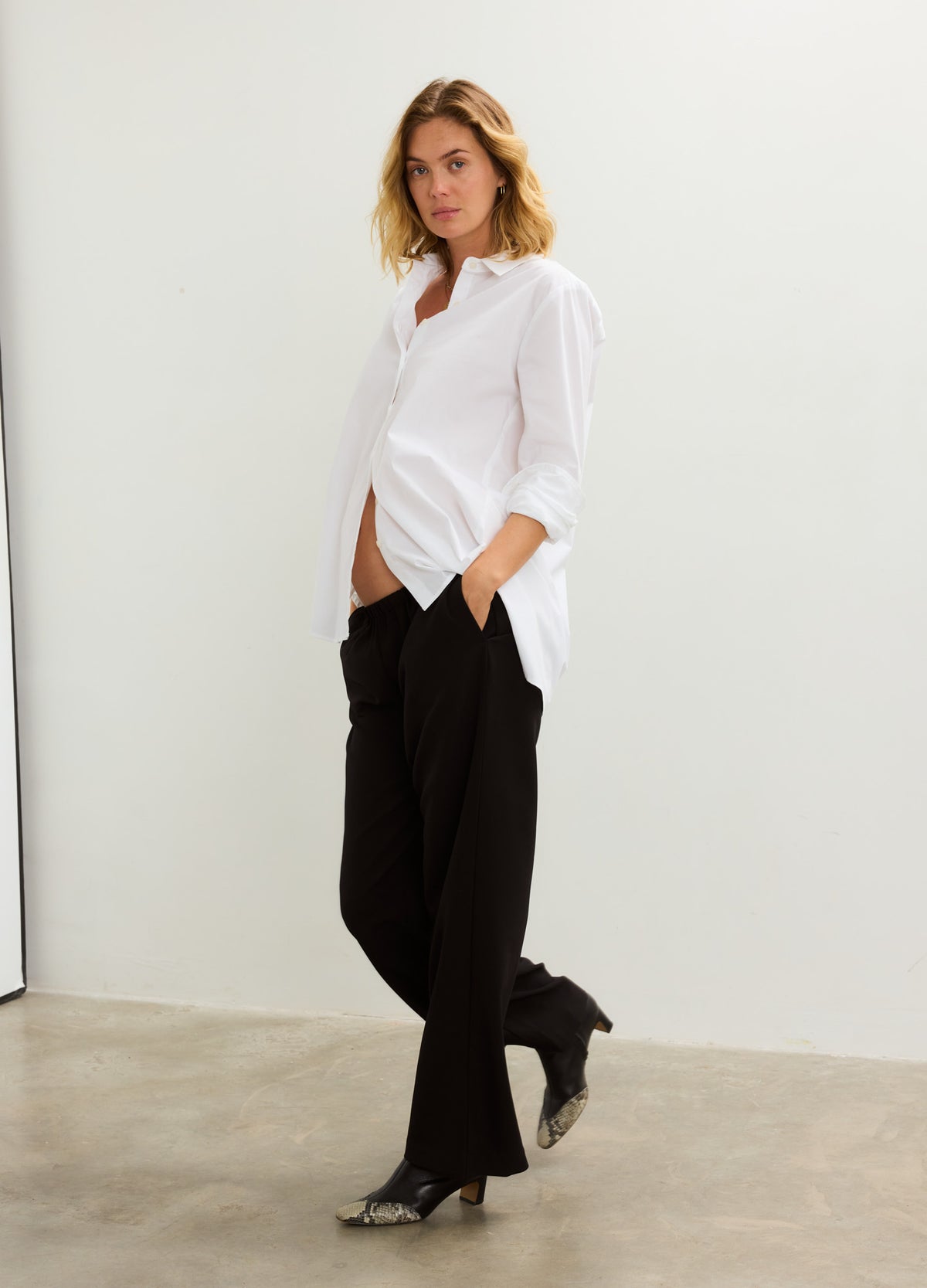 White maternity button-down shirt with long sleeves paired with black relaxed-fit trousers.