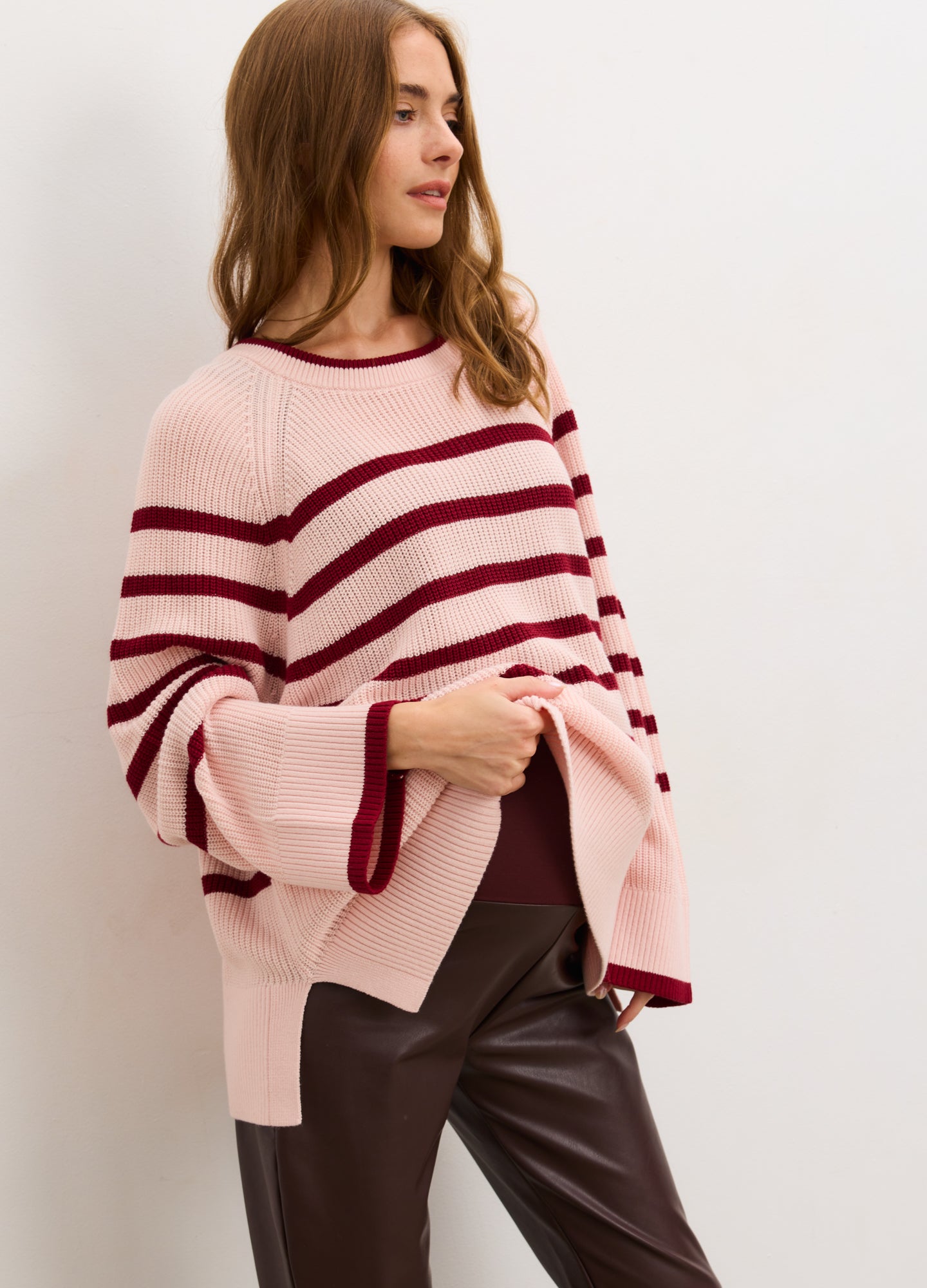 Pregnant woman wearing a pink and red striped sweater against a white background

